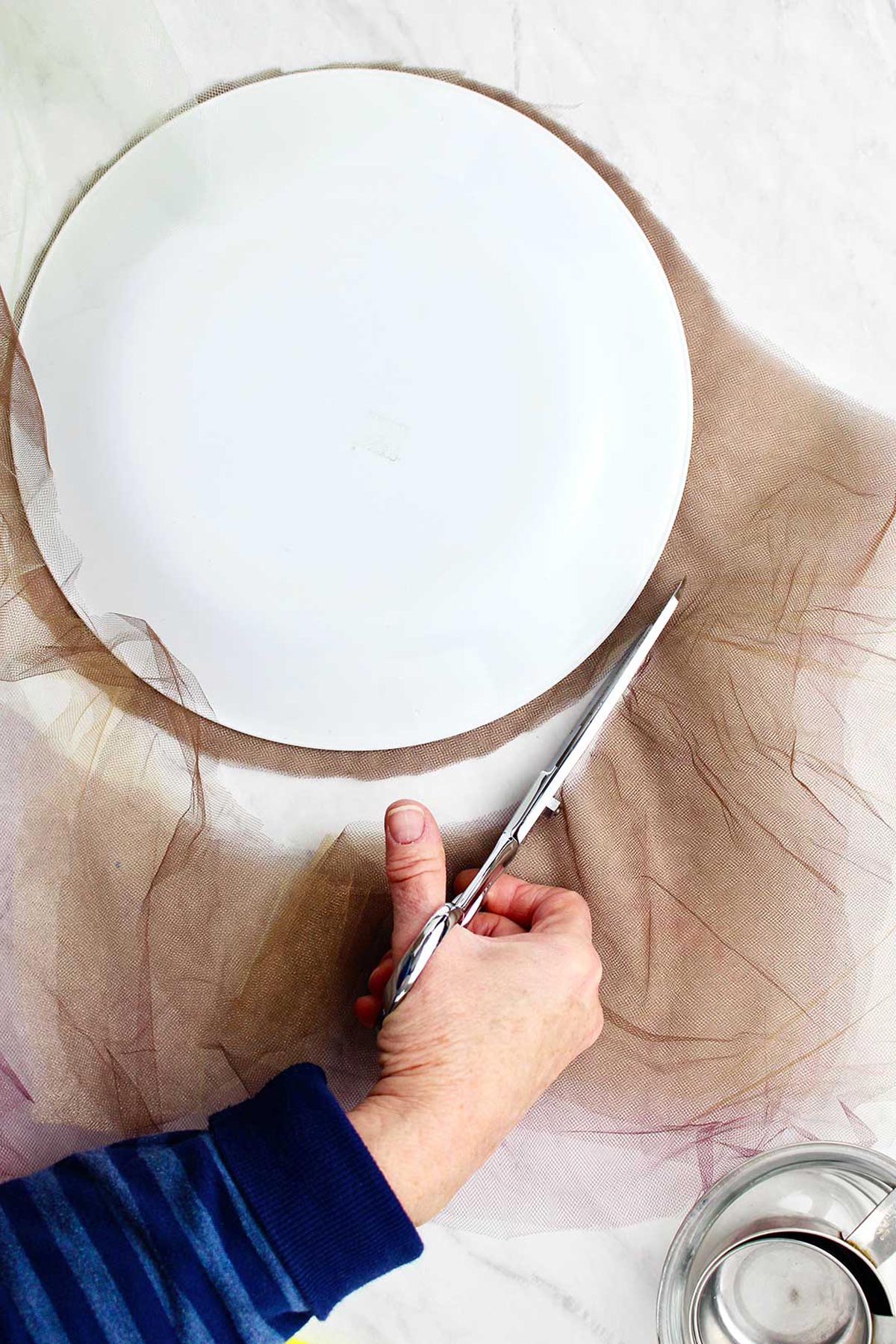 Hand cutting brown tulle in a circle with scissors.