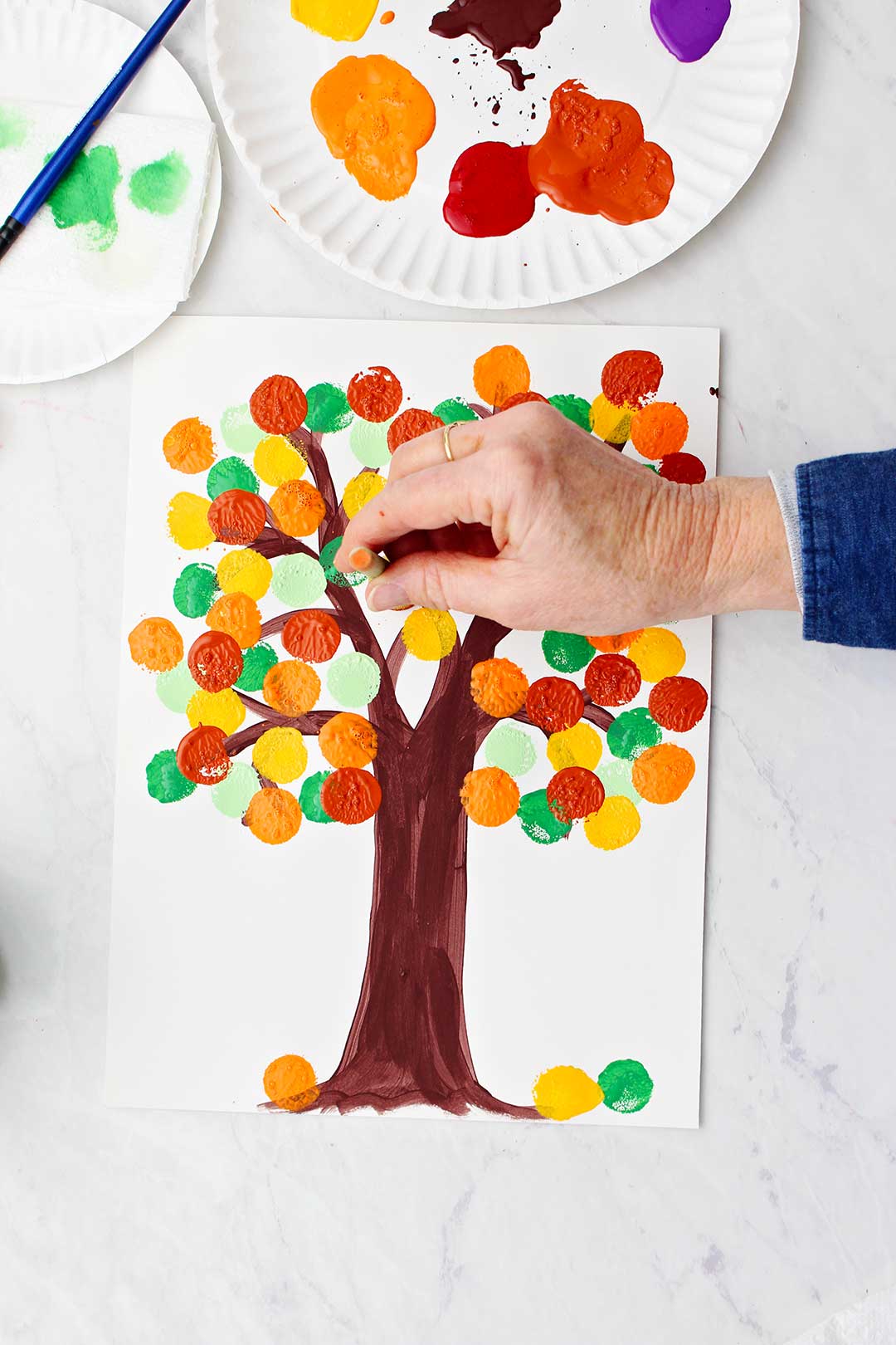 Hand stamping orange leaves on tree painting using circular stamping tool.