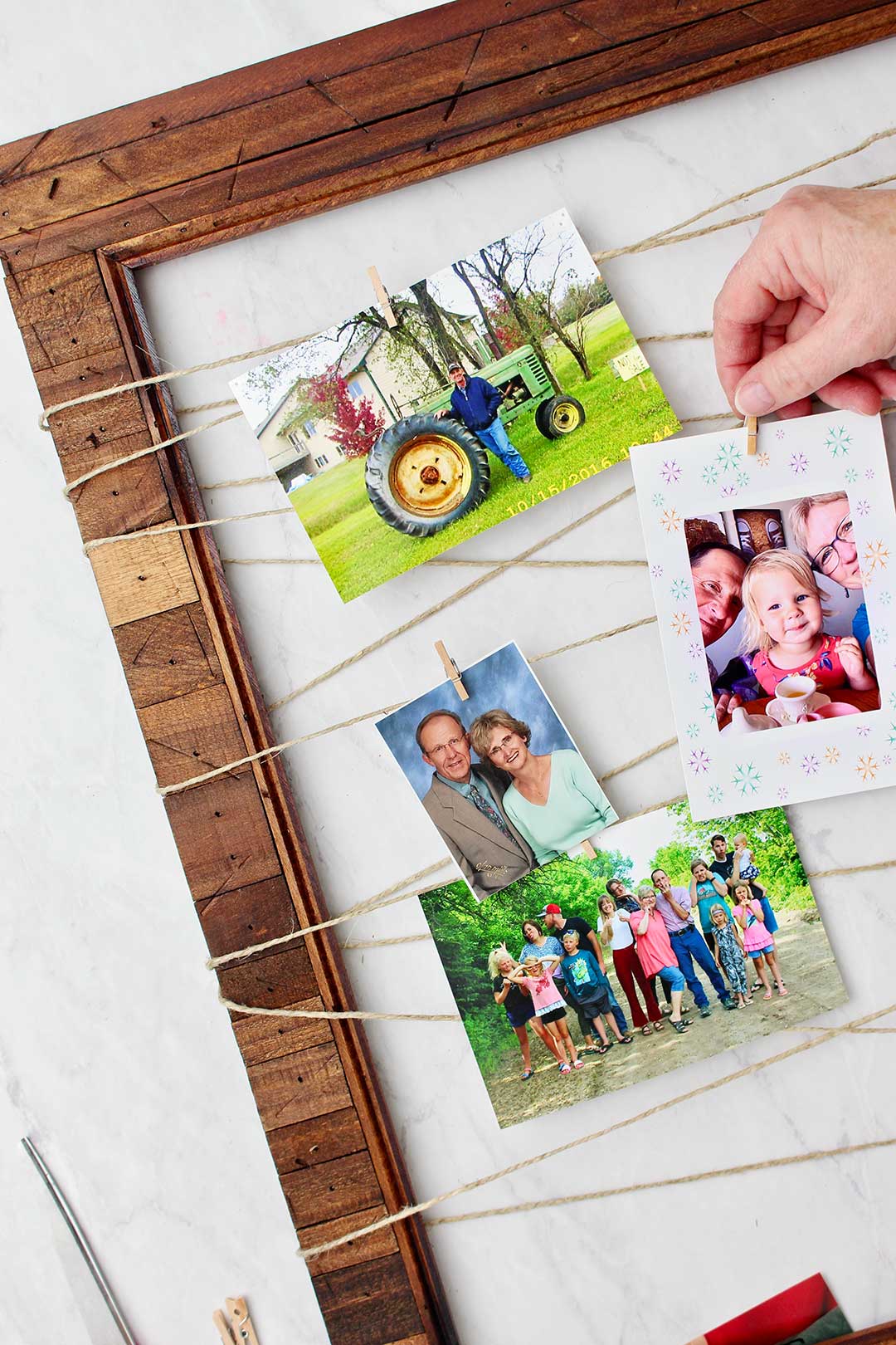 Hand clipping a photo of grandparents with toddler granddaughter on Upcycled Picture Frame with mini clothes pin.