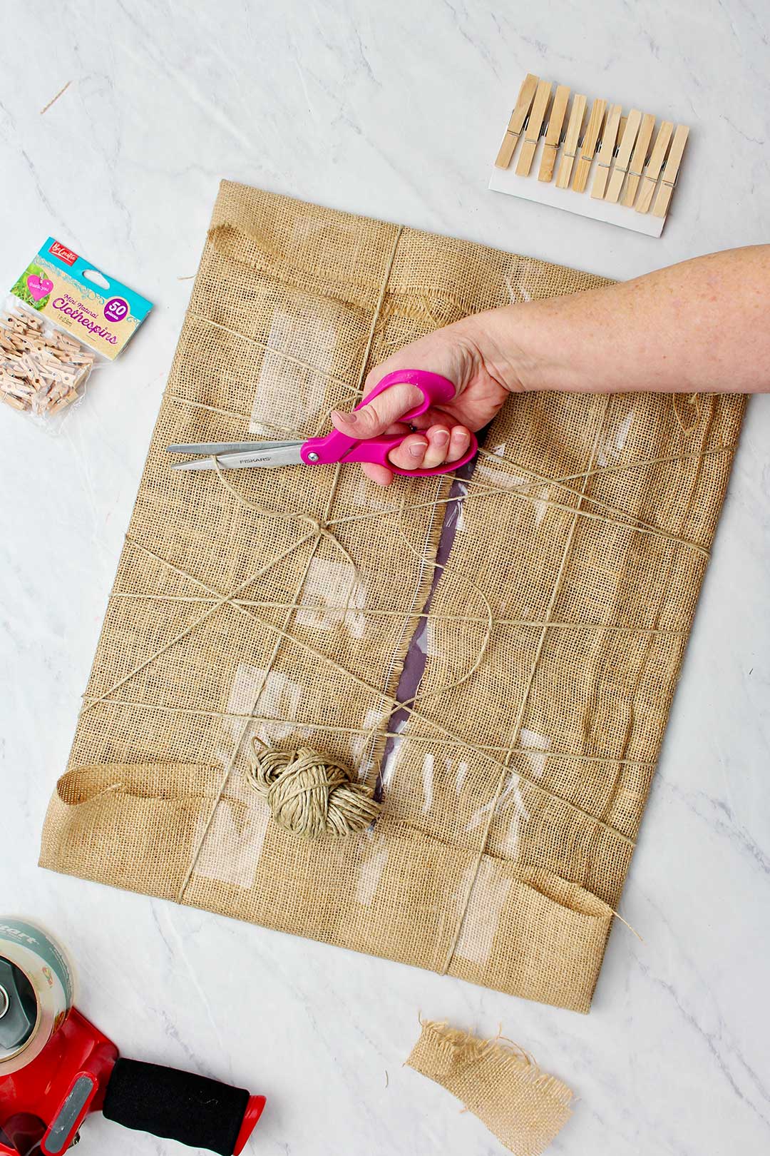 A hand cutting piece of twine showing the back of the insert with criss crossed twine over burlap.