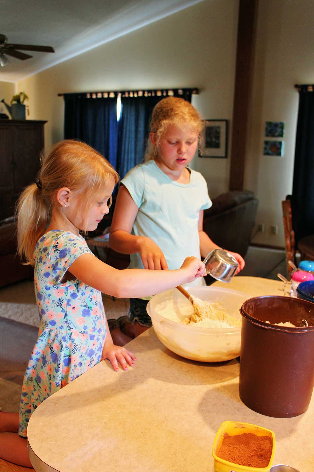 Two girls add flour to a bowl at the kitchen counter.
