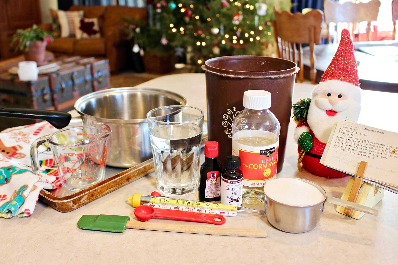 All components and ingredients for cinnamon candy on a counter top with Christmas tree in the background.