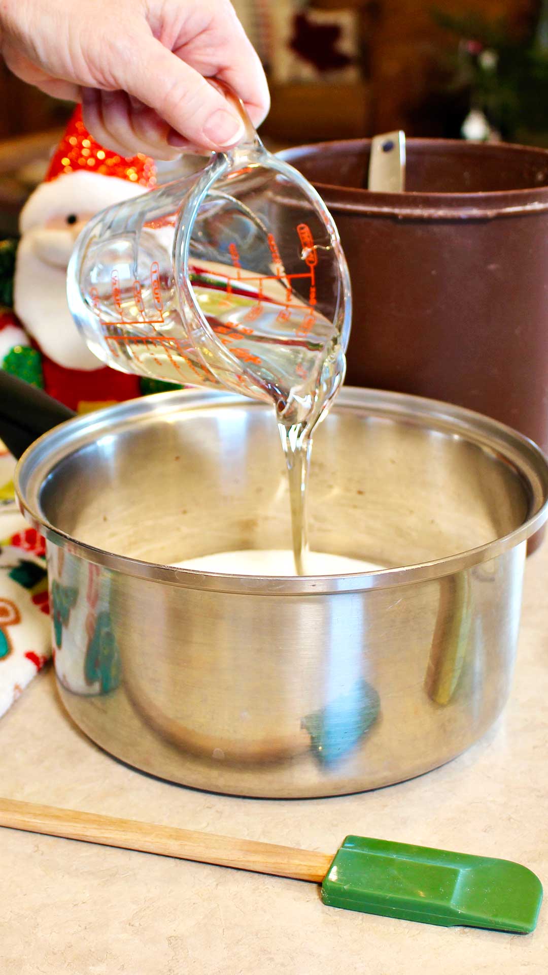 Hand pouring corn syrup into a pot of sugar on the counter top.