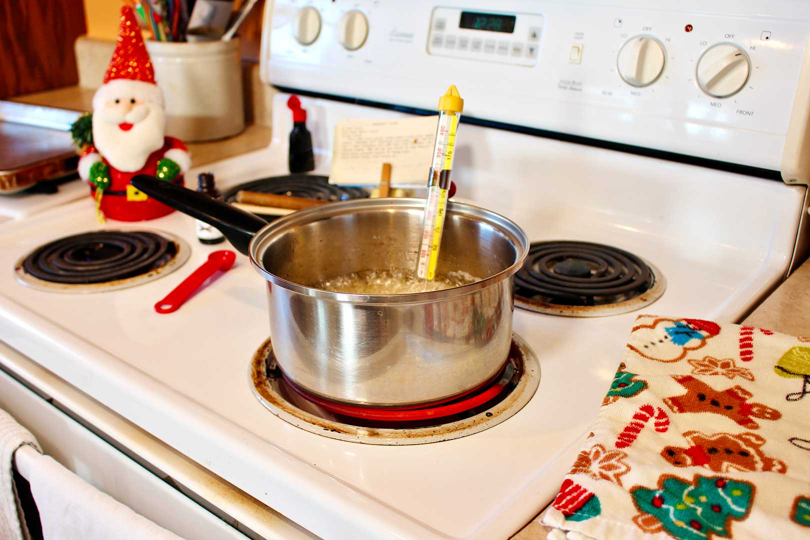 Saucepan of bubbling sugar on the stove with a candy thermometer resting in it.