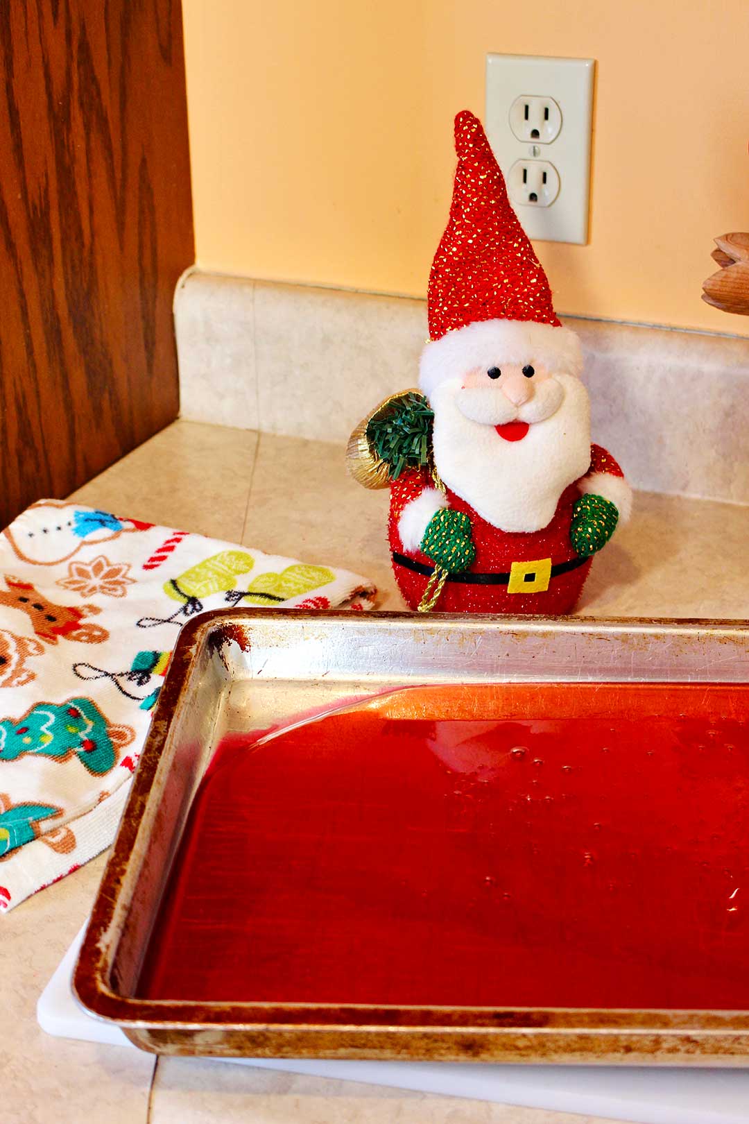 Cookie sheet of cinnamon candy rests on a counter top with a Santa decoration in the background.