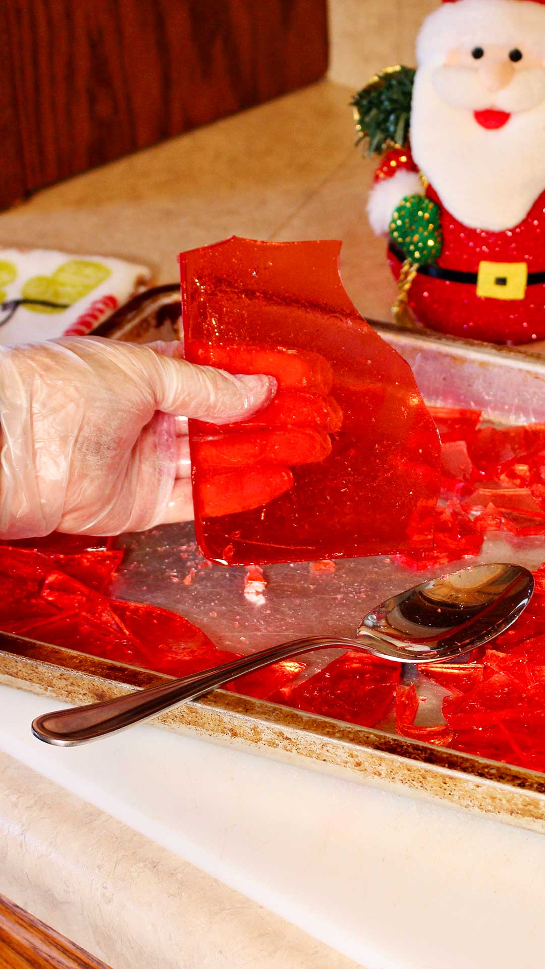 Hand holding large piece of broken homemade cinnamon candy with a Santa decoration in the background.