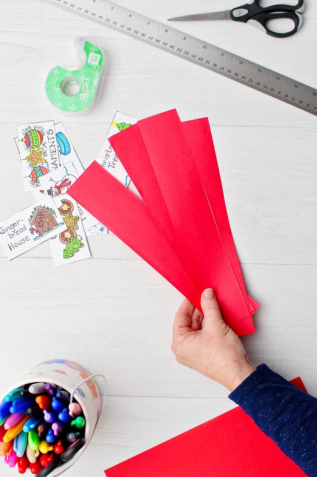 Hand holding strips of red paper to make into headbands to hold different Christmas cards for game.