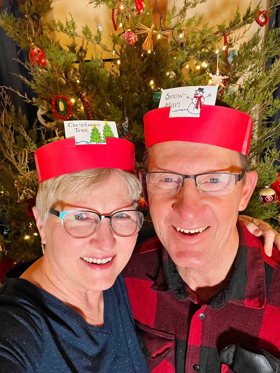 Nana and Papa with DIY headband game on heads in front of a decorated Christmas tree.
