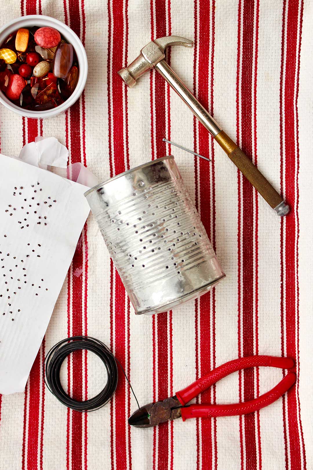 Tin can punched through with snowflake design with beads, hammer, wire and wire cutters near by.