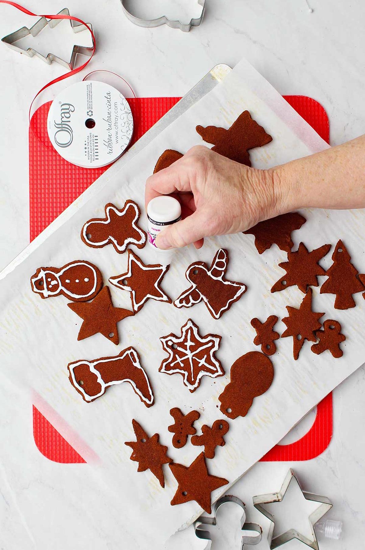 Hand decorating cinnamon applesauce ornaments with white paint on parchment covered cookie sheet.