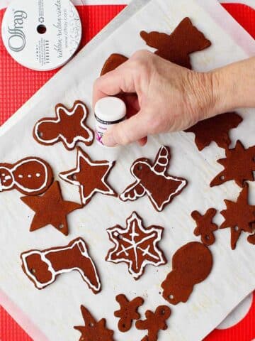 Hand decorating cinnamon applesauce ornaments with white paint on parchment covered cookie sheet.