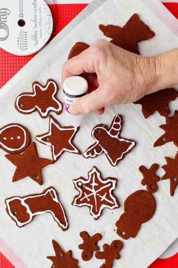 Hand decorating cinnamon applesauce ornaments with white paint on parchment covered cookie sheet.