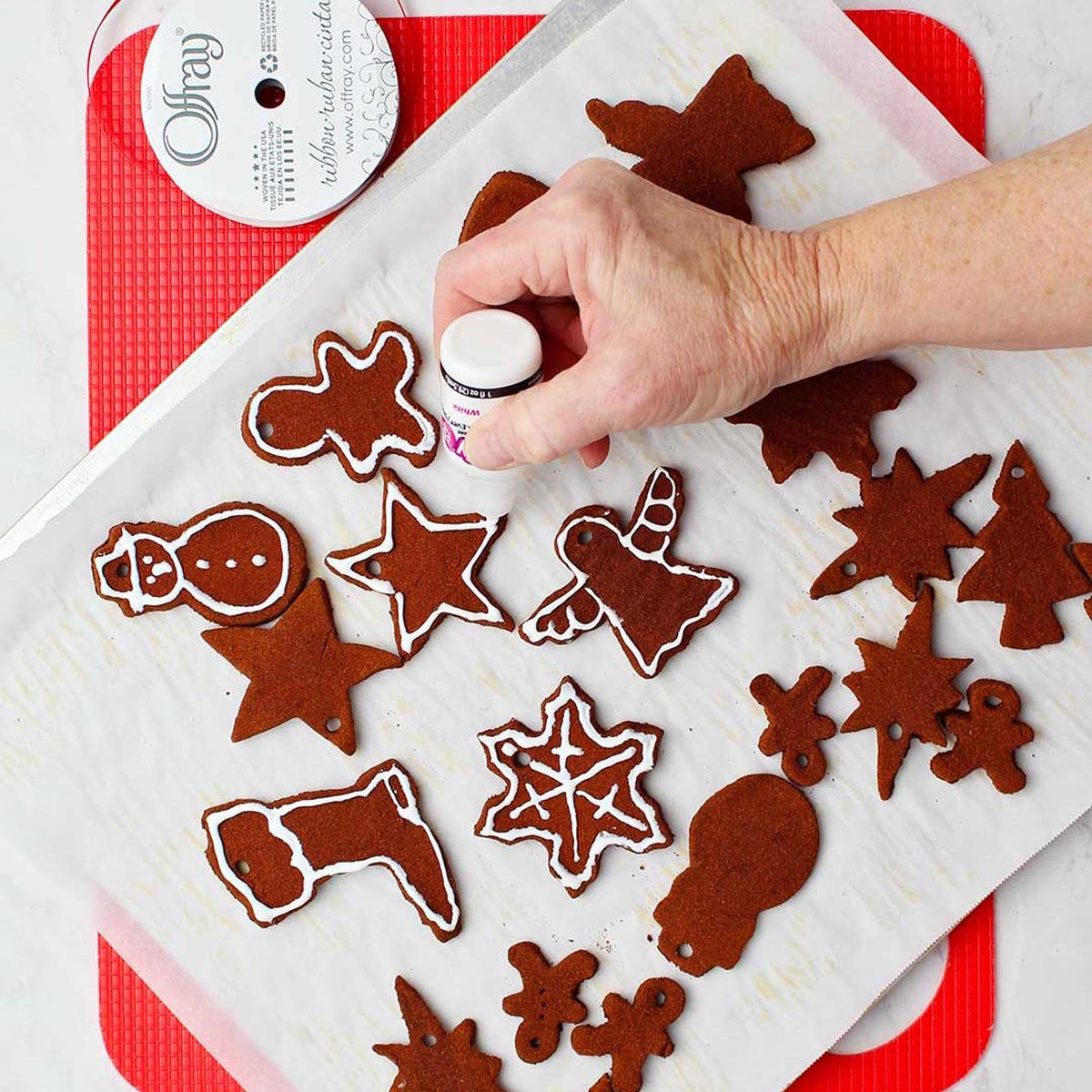 Hand decorating cinnamon applesauce ornaments with white paint on parchment covered cookie sheet.