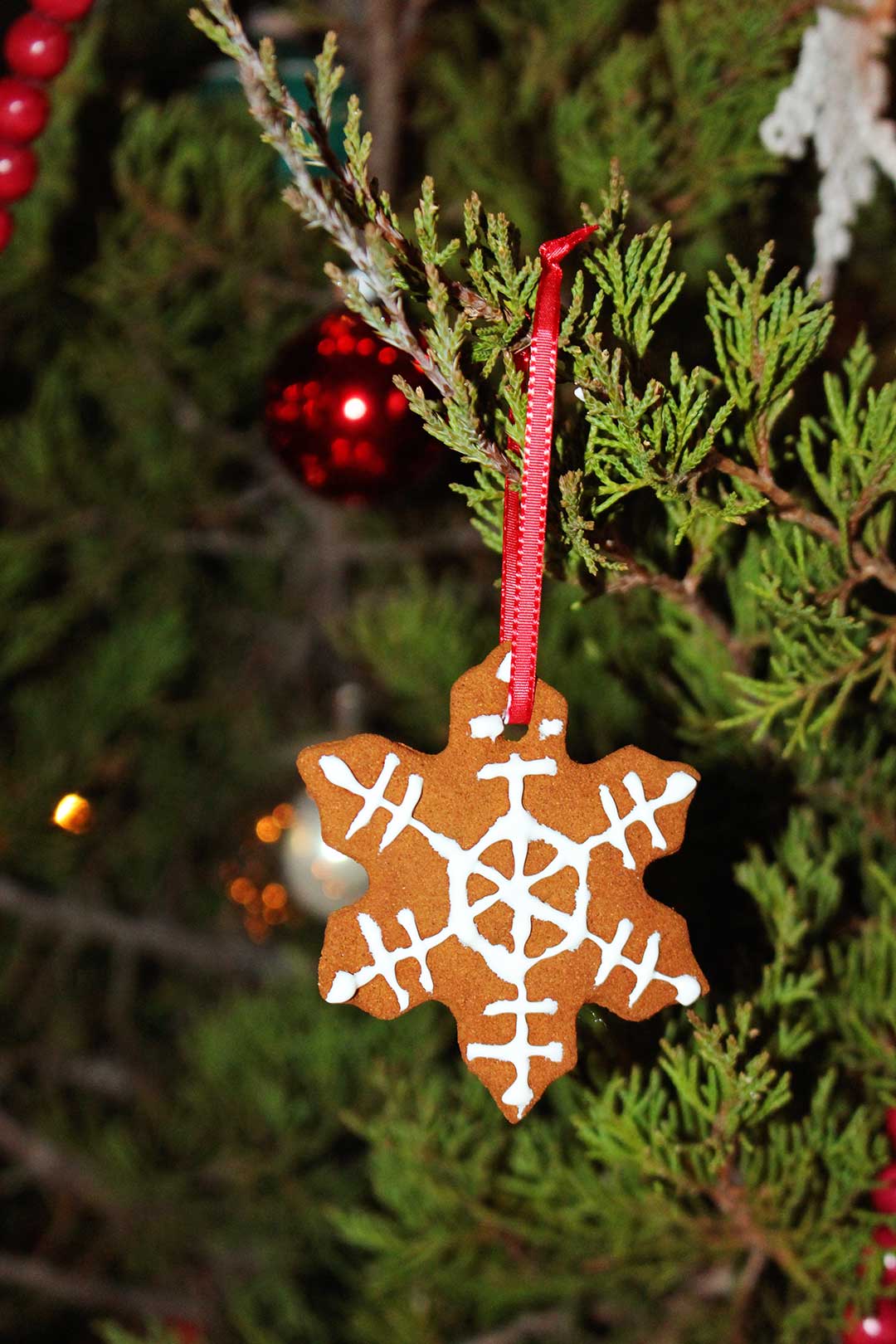 Completed snowflake shaped cinnamon applesauce ornament hanging from Christmas tree.