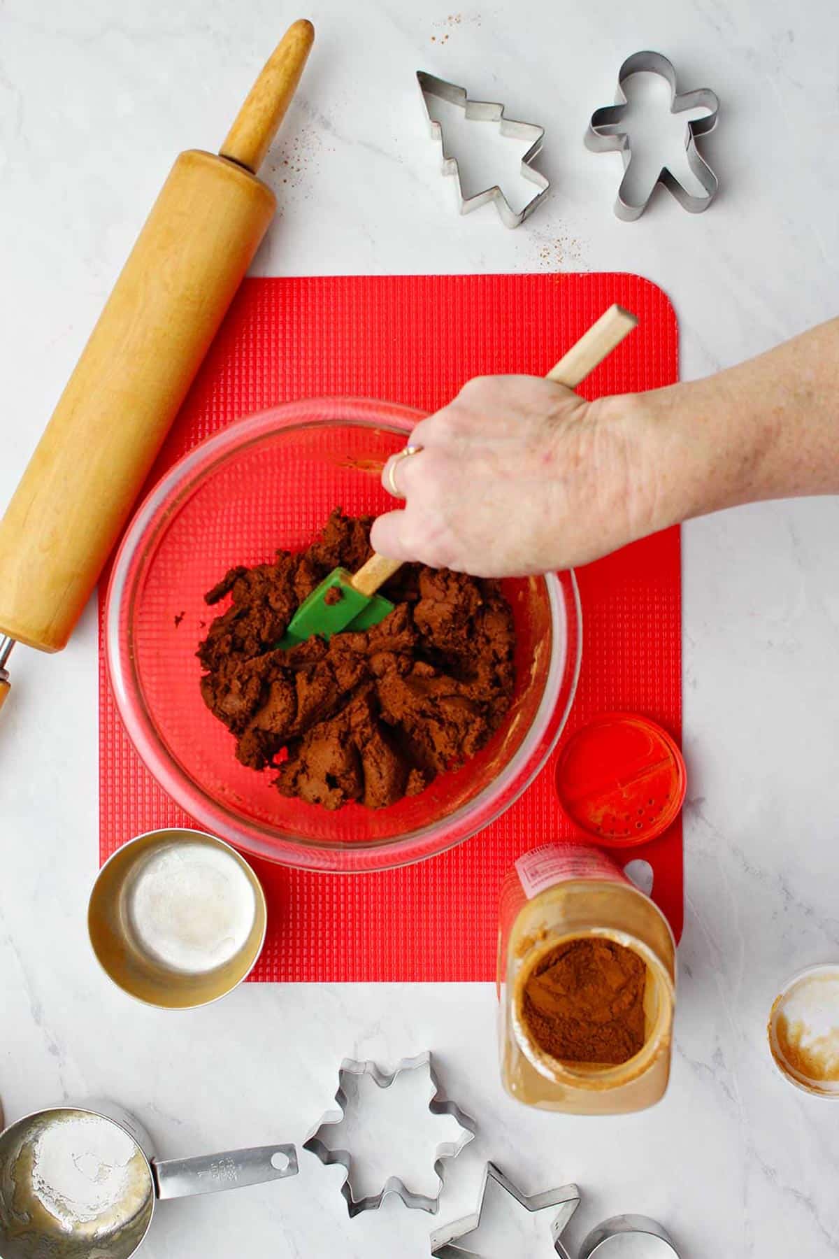 A hand mixing the dough after the adding of cinnamon to the applesauce with supplies around it.