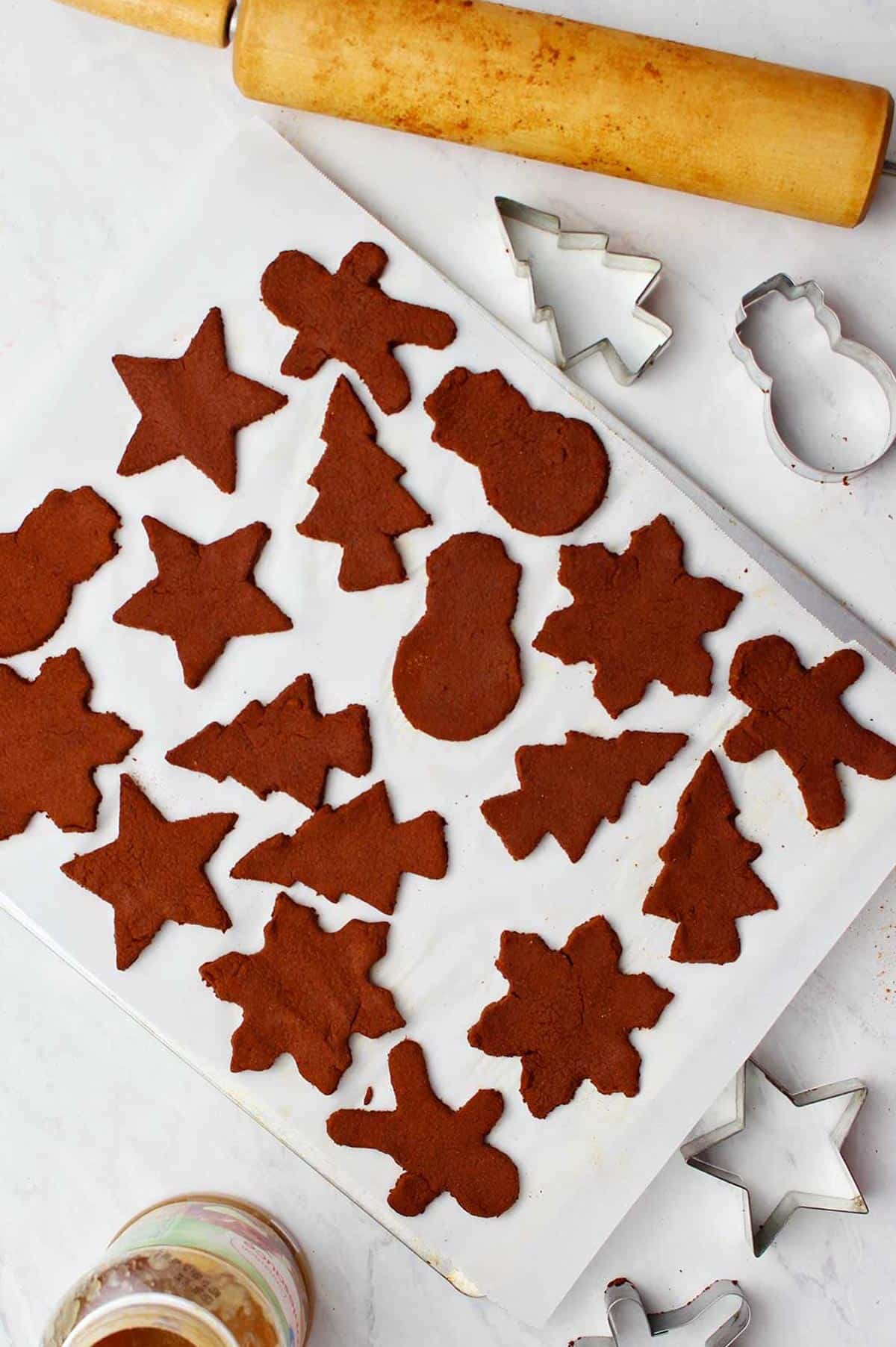 Cookie sheet with parchment on counter with Christmas ornaments ready for the oven with various supplies near by.