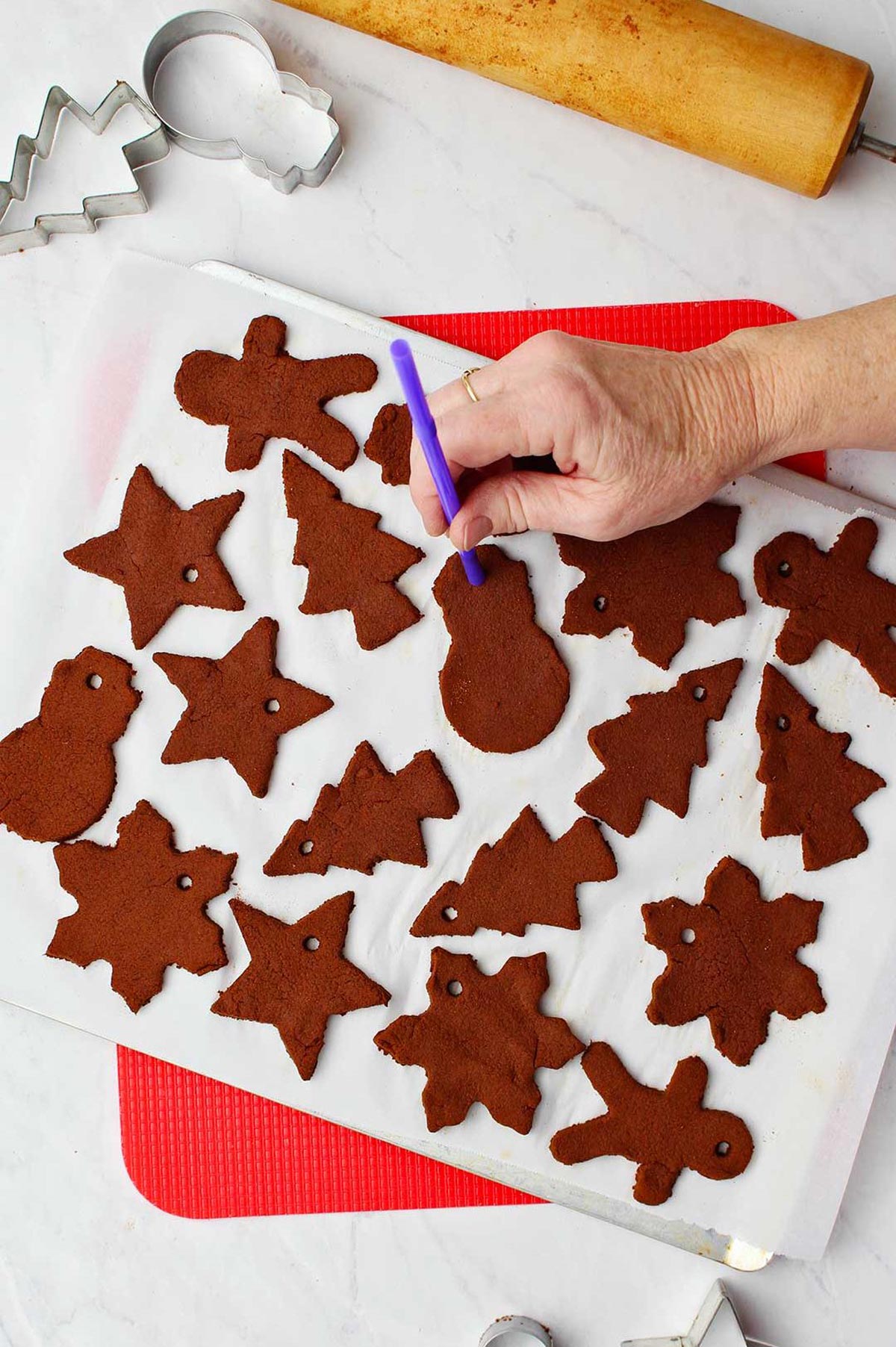 Hand holding purple straw punching holes at the top of the ornaments for hanging purposes.