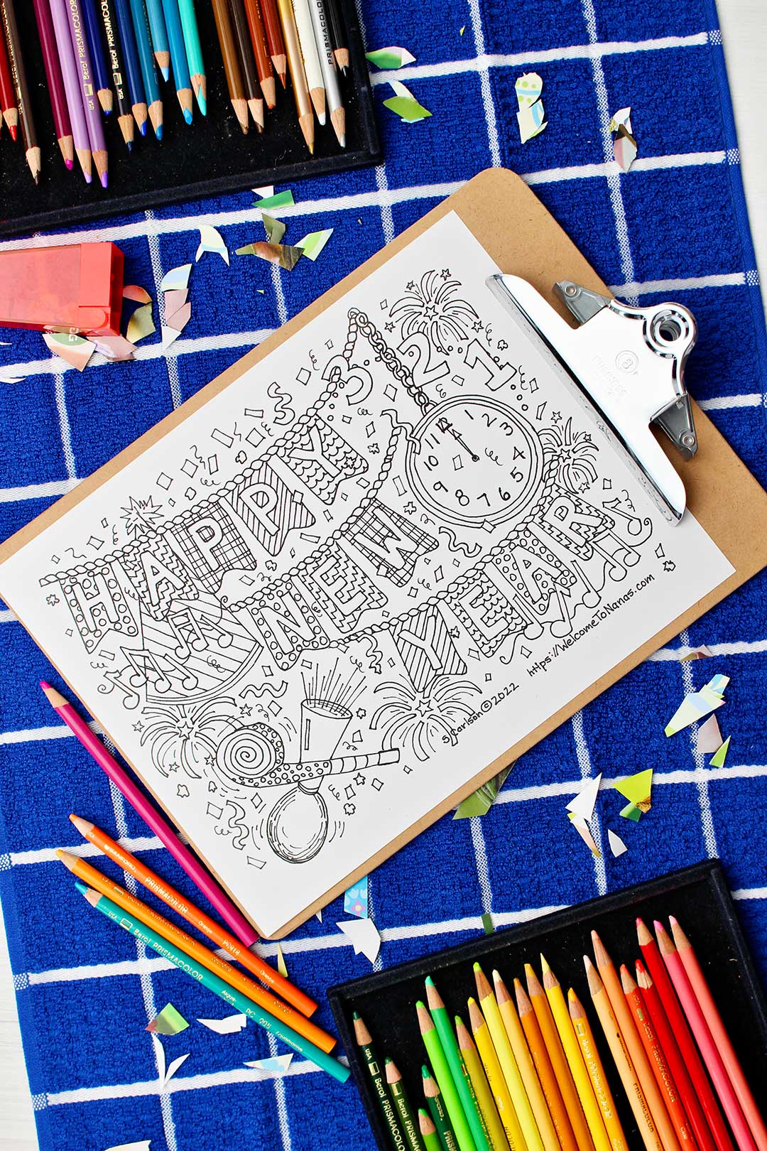 Uncolored New Year's Coloring Page on a blue checkered place mat with colorful colored pencils and confetti scattered about.