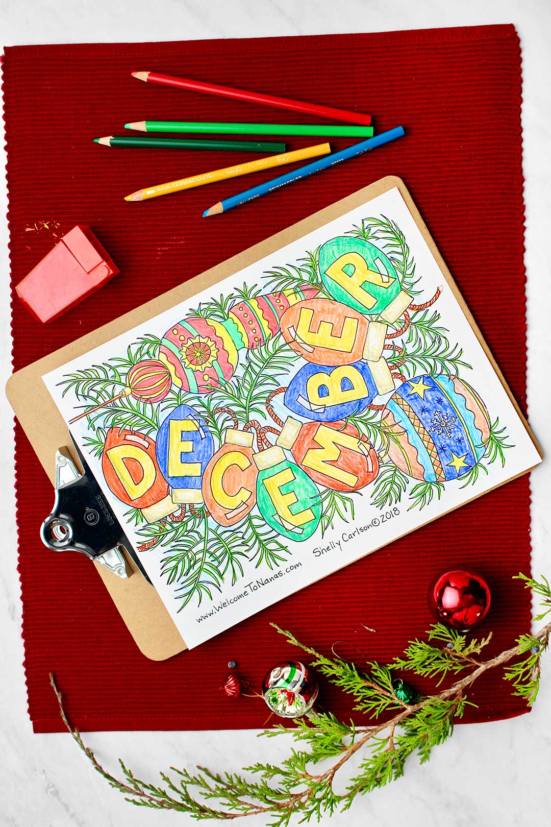 Finished December coloring page resting on a red placemat with holiday decorations and colored pencils.