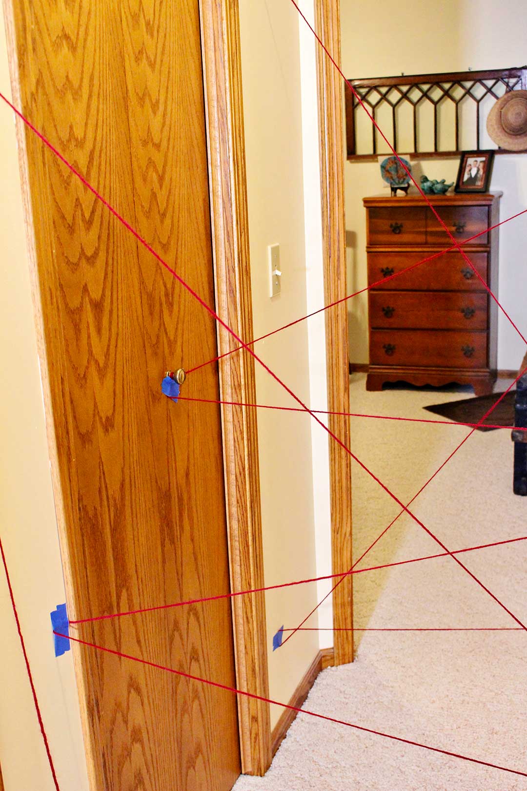 Red yarn taped to a closet door in a hallway in a yarn maze with a view of a bedroom with dresser and wall hanging.
