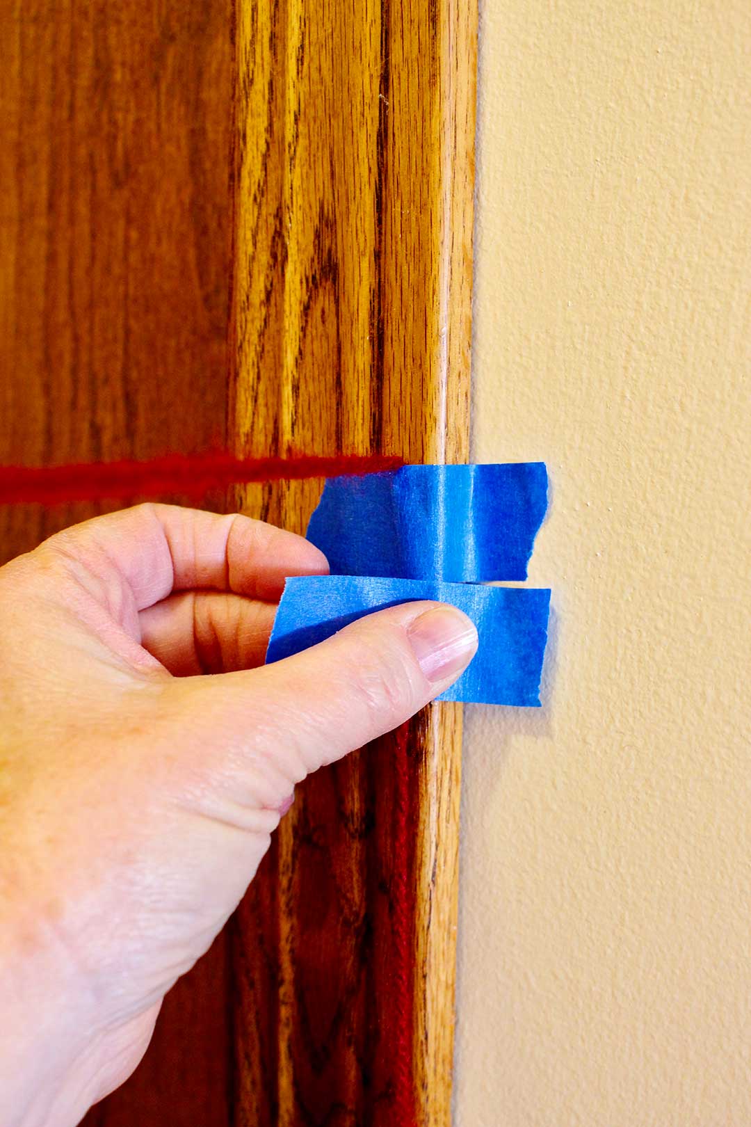 Close up view of person taping red yarn to a door frame with blue painters tape.