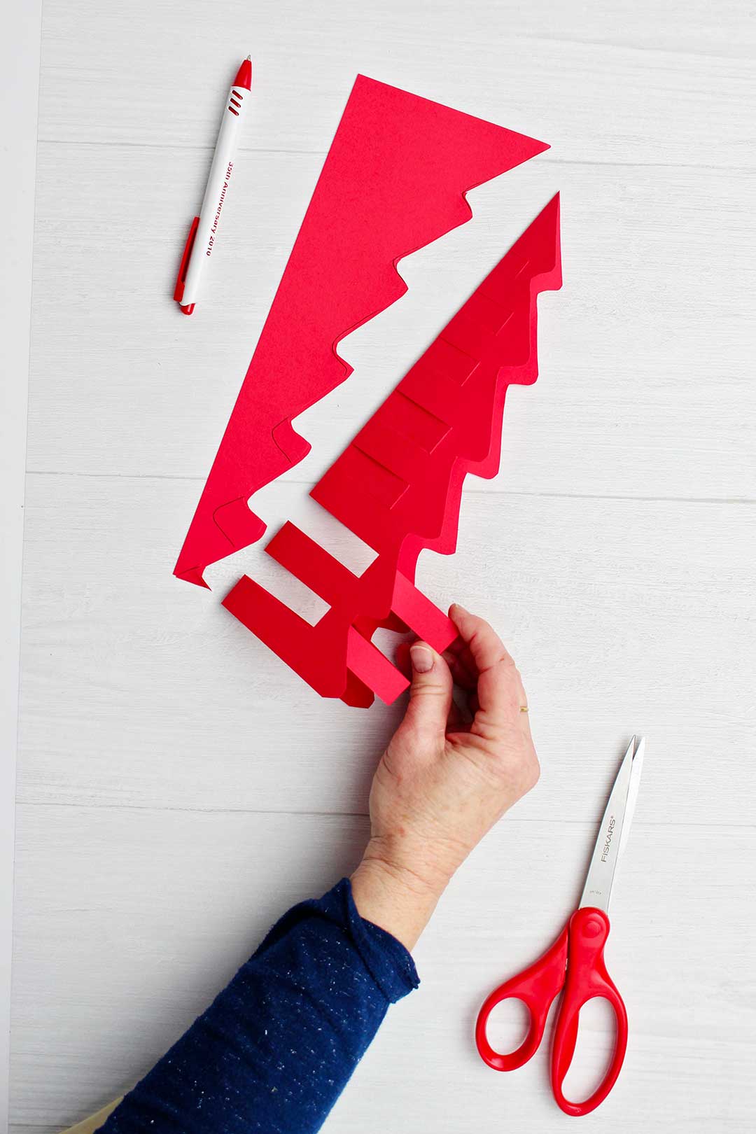 Hand showing where to cut out on red origami tree.