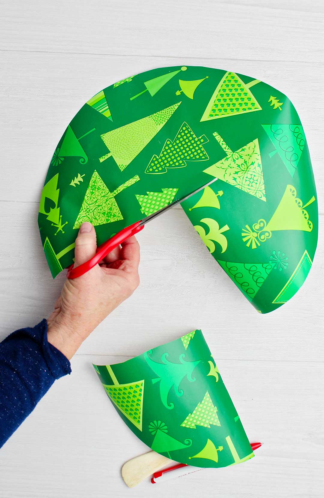 Hand cutting section out of a circular cut out of patterned green tree paper.
