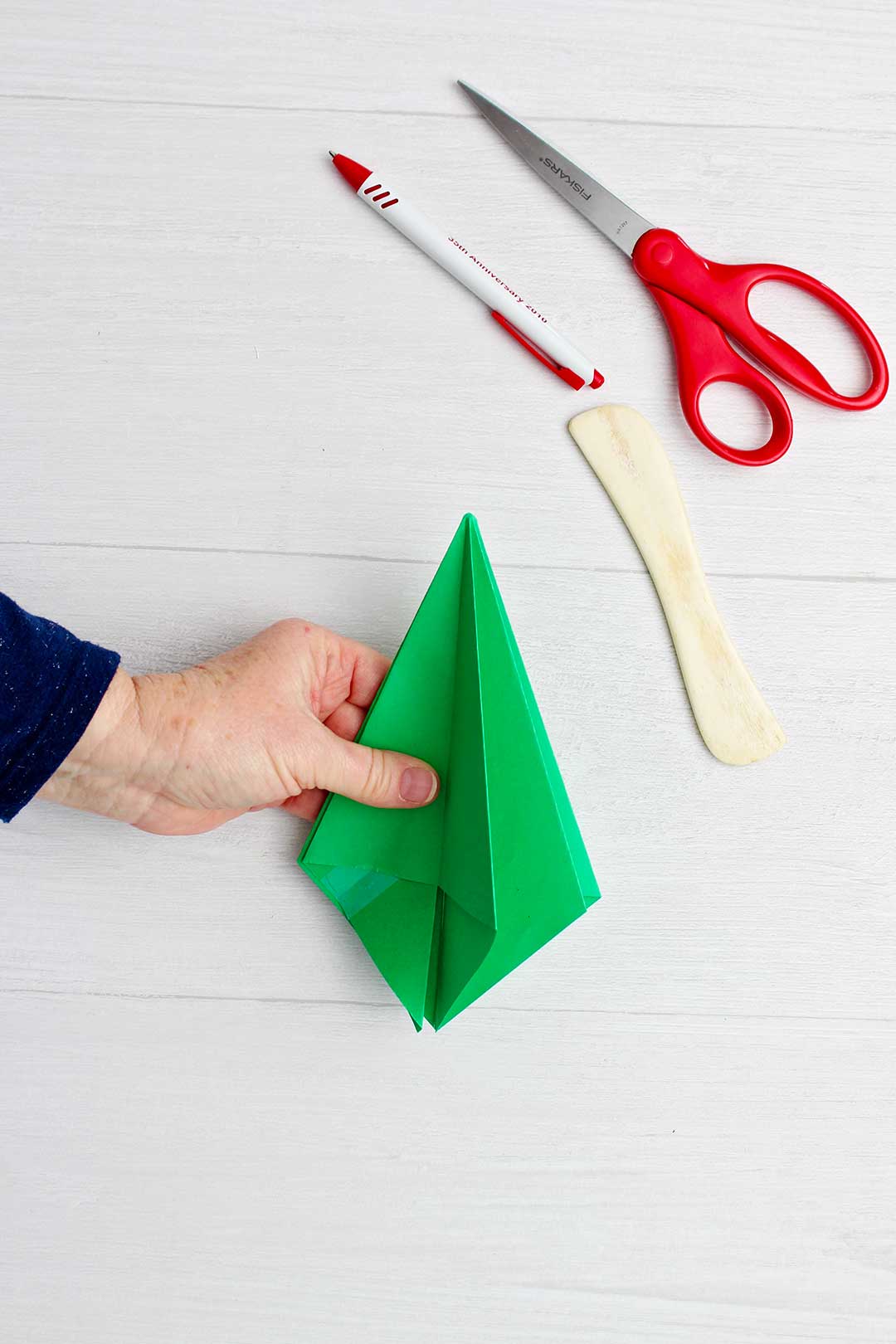 Hand holding green origami tree after folding in corner pieces.