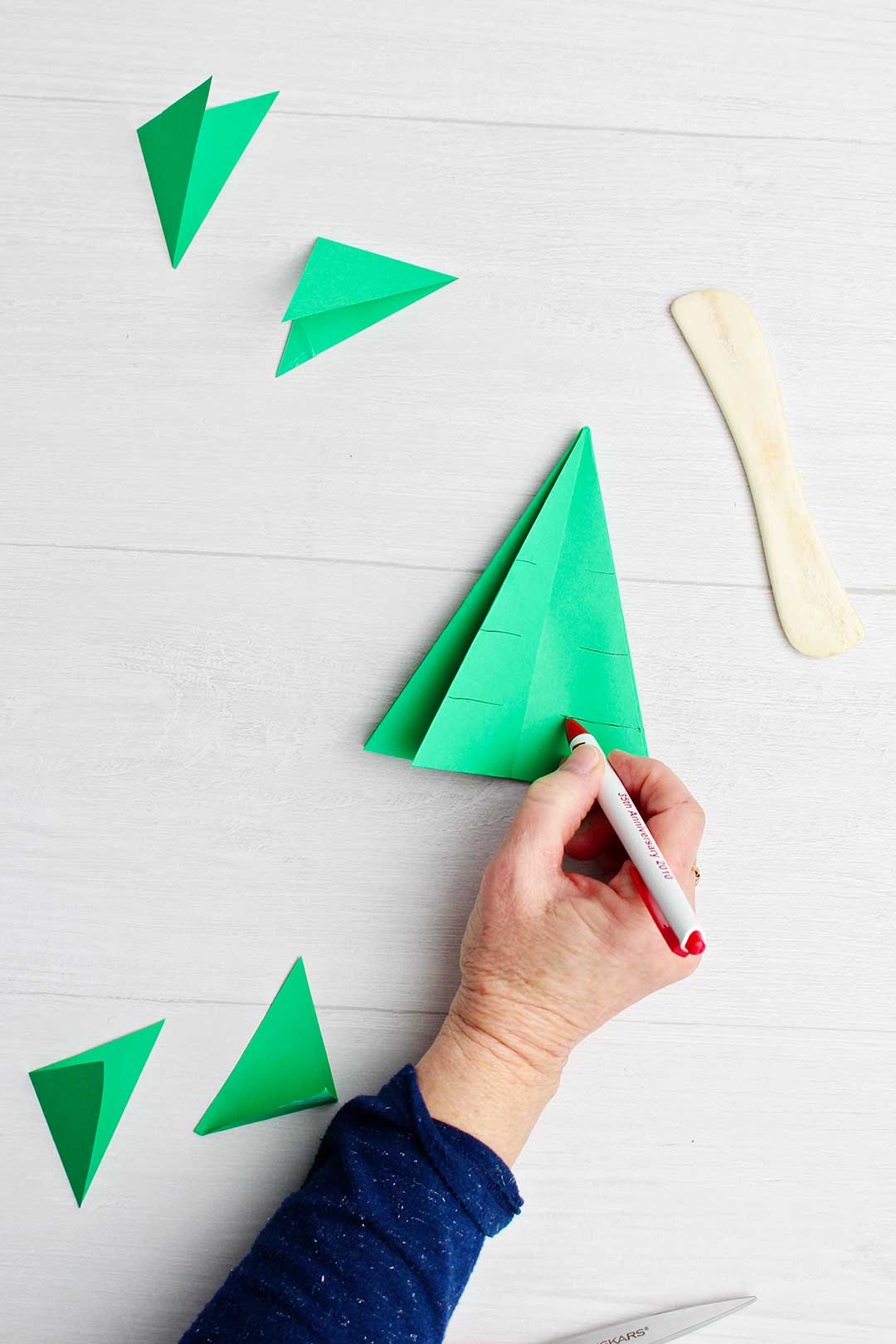 Hand drawing pen lines on green origami tree to show where to cut.