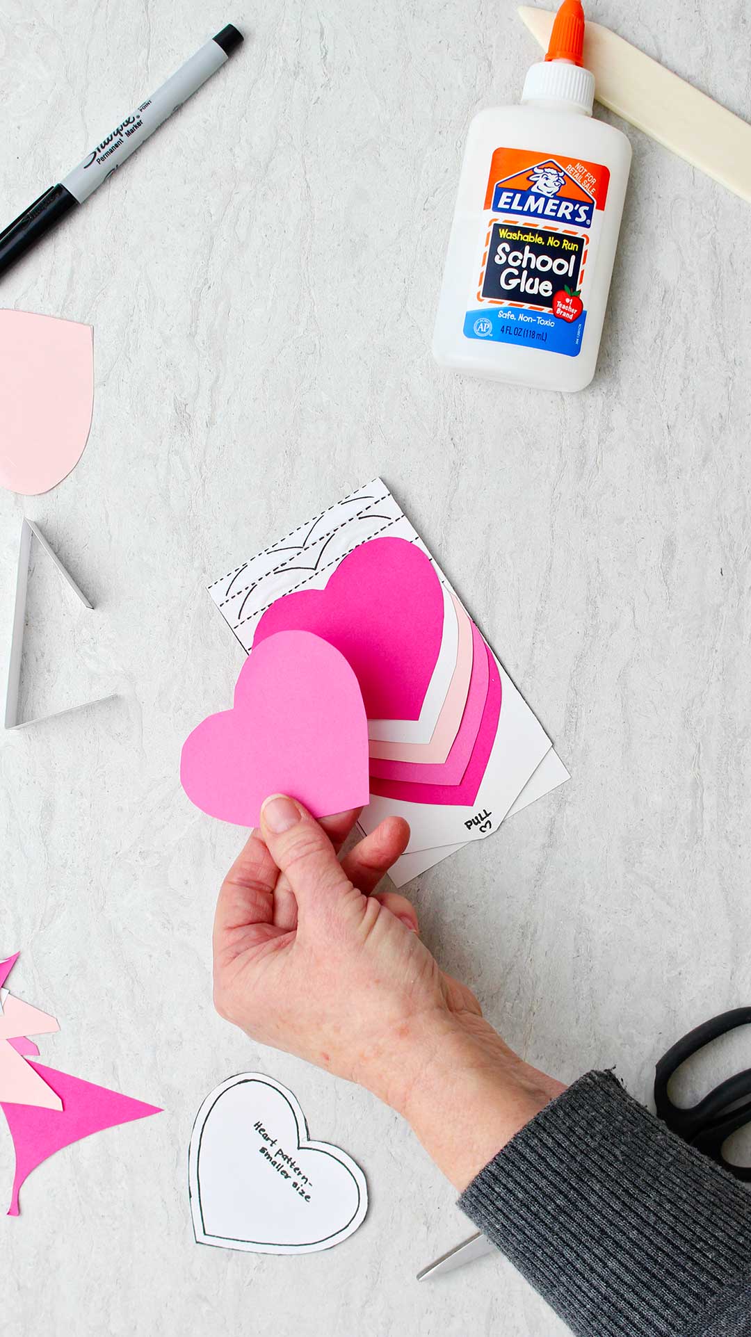 Hand holding a pink heart getting ready to line it up on the template for the waterfall card.