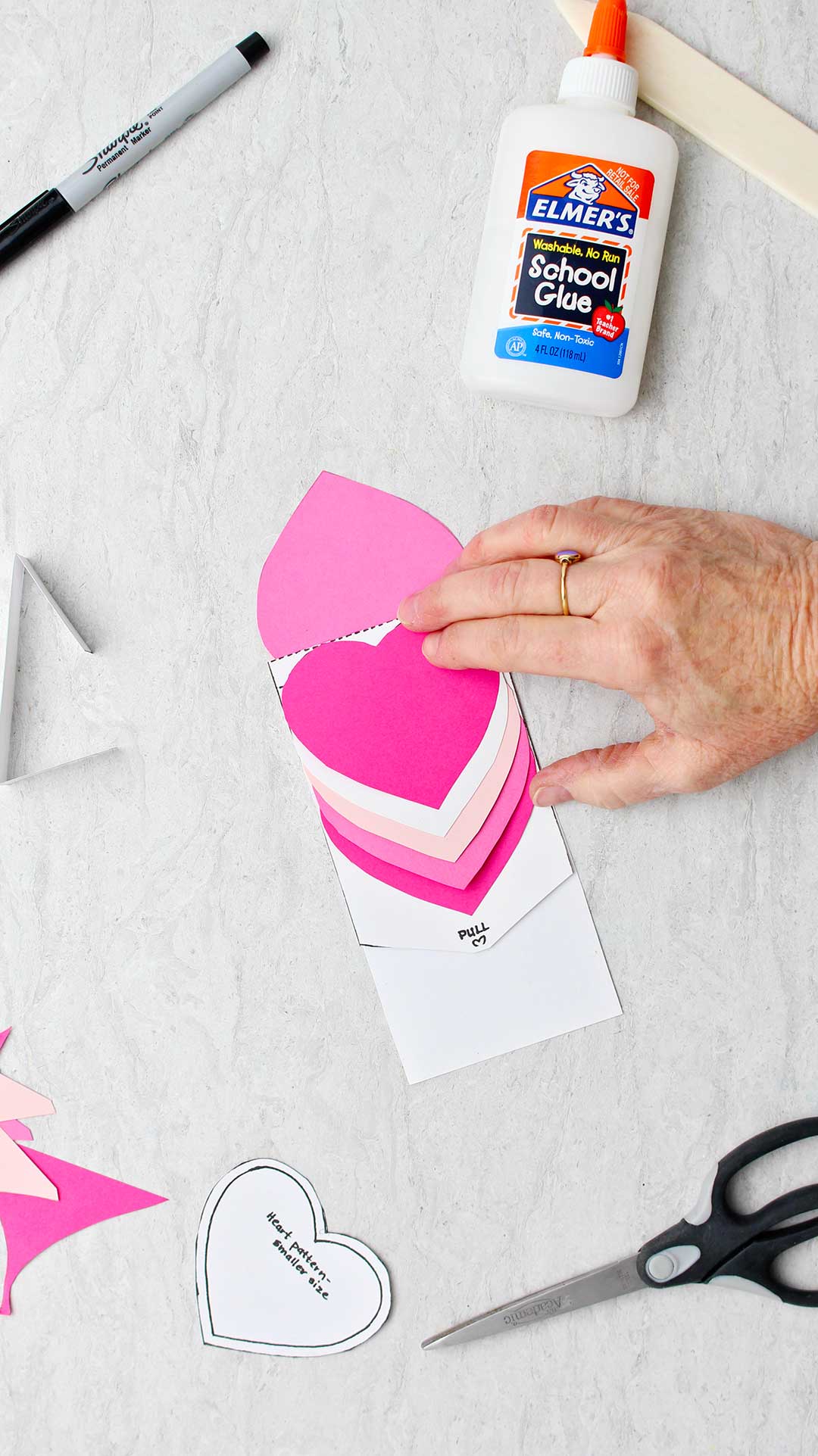Hand pressing down on bright pink heart to secure it to the card.