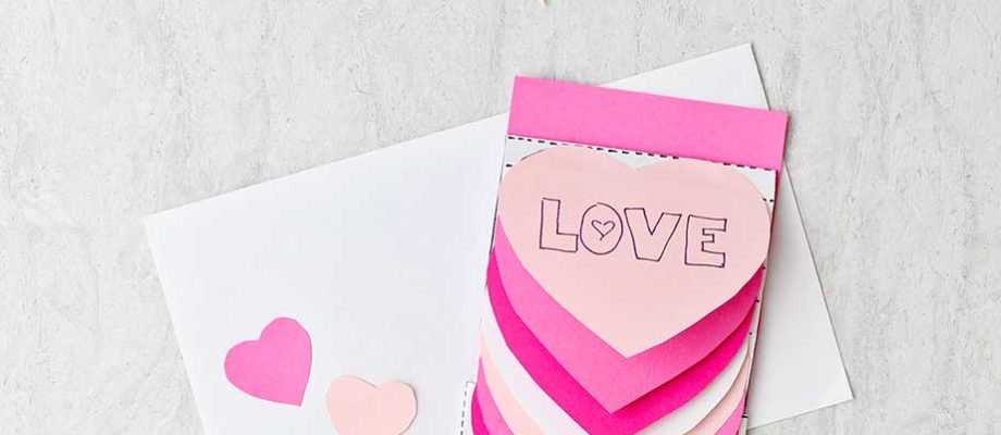 Completed waterfall heart card in different shades of pink with supplies near by.