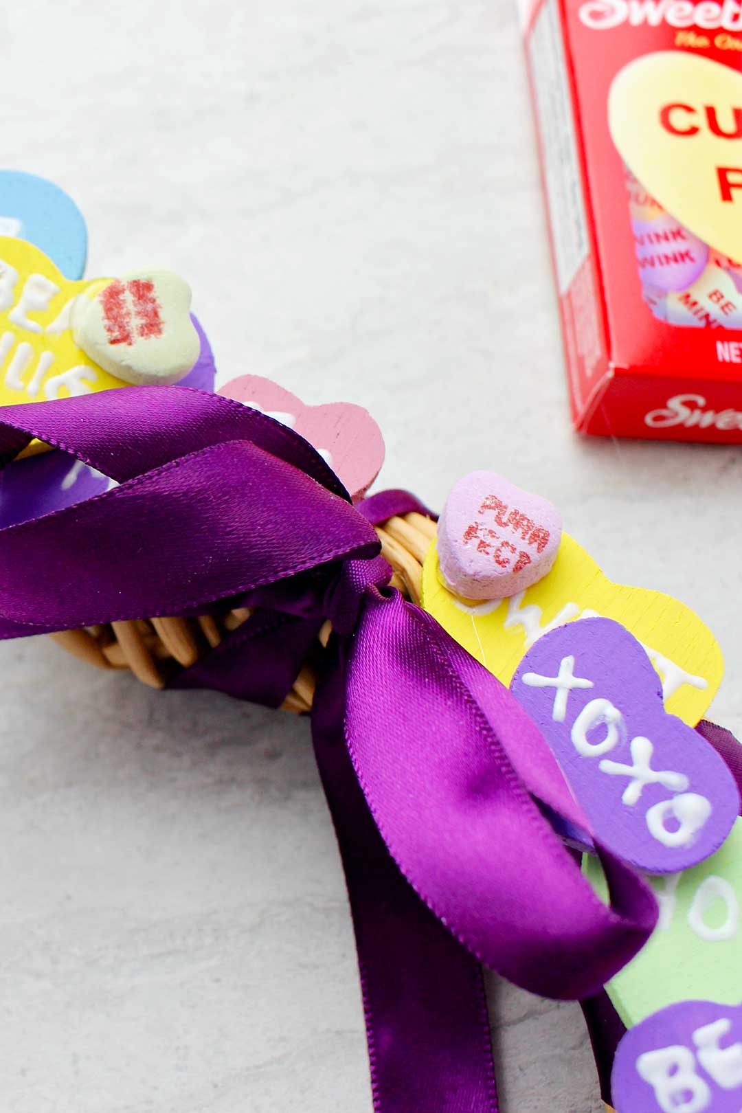 Close up shot of the bow tied with purple satin ribbon on Conversation Heart Wreath.