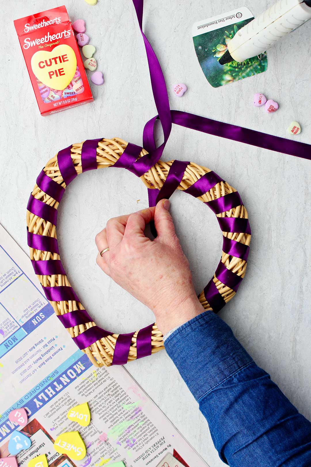 Hand lacing purple satin ribbon around heart shaped wreath.