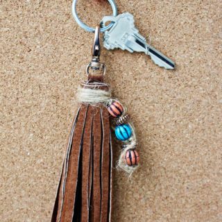 Close up of leather tassel keychain with orange and blue beads resting on a cork board.