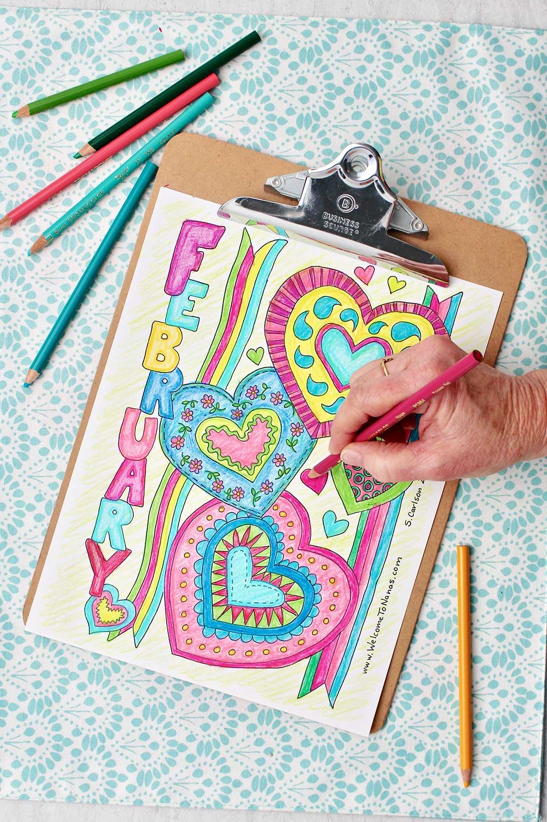Hand coloring a heart pink on mostly finished coloring page.