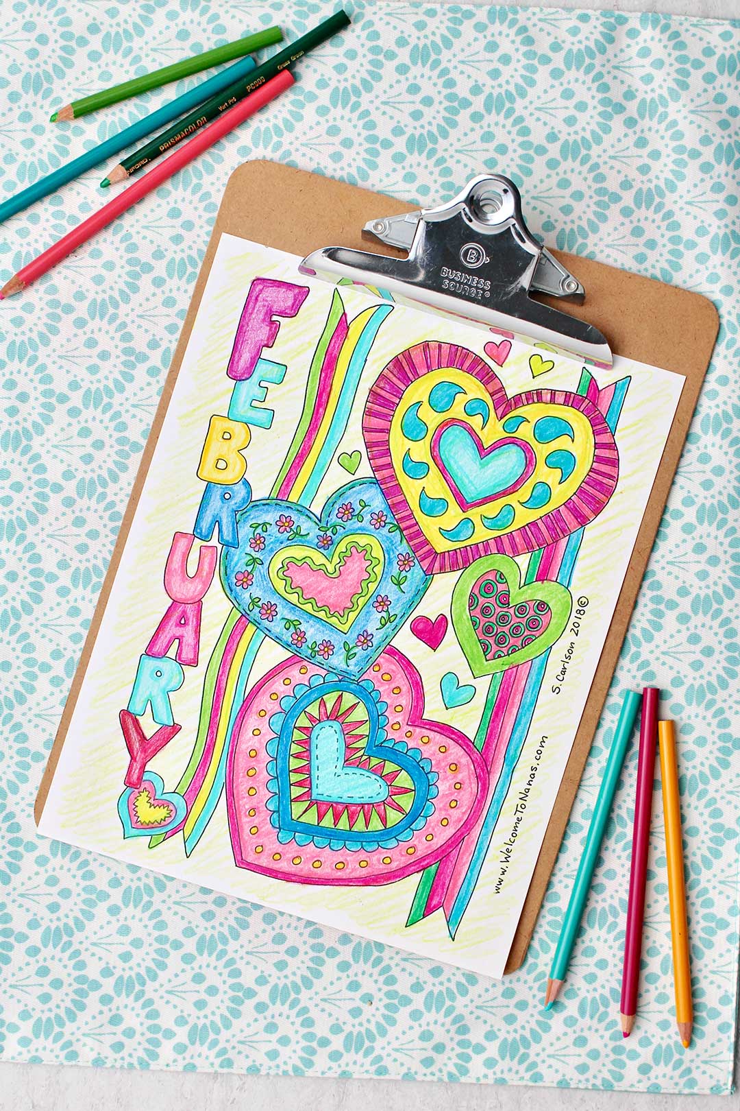 Completed February Coloring Page on a clip board with colored pencils near by.