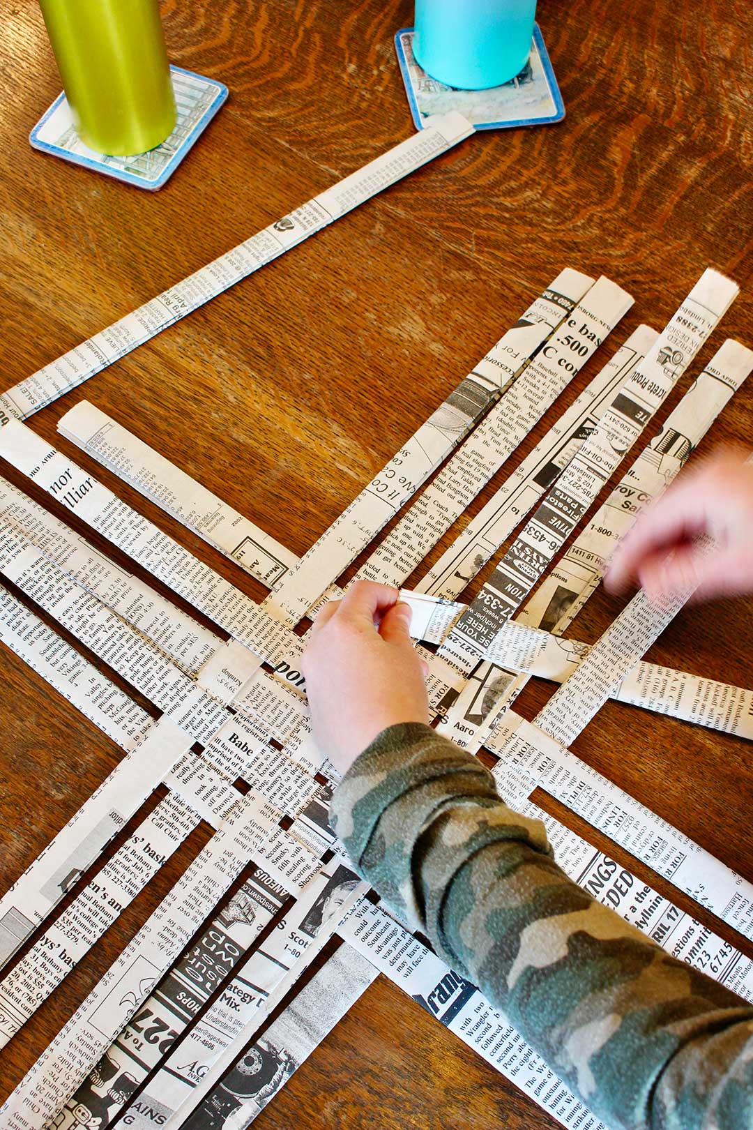 Child's hands arranging strips of folded newsprint to make the base of the woven newspaper basket.