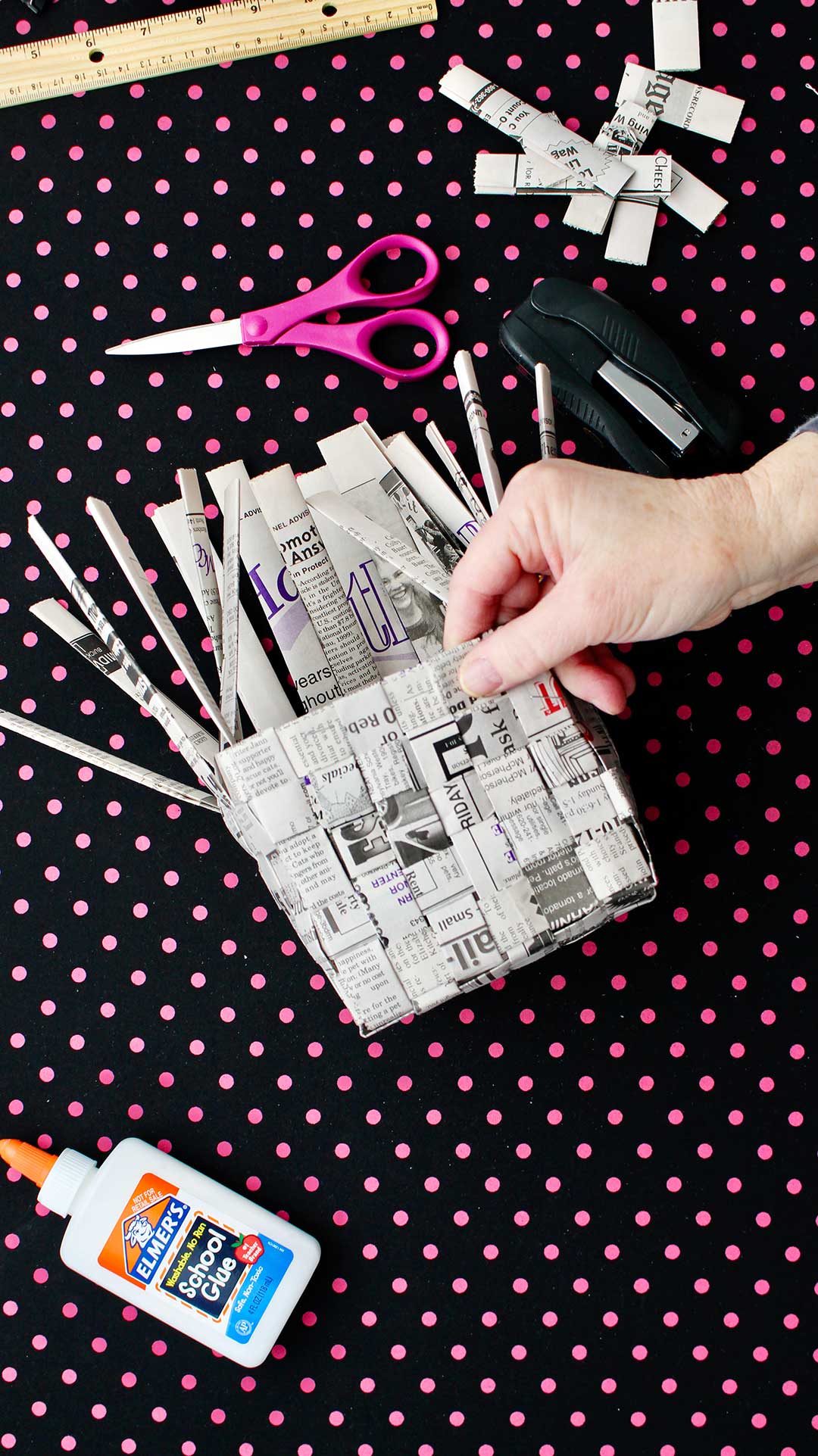 Hand showing glueing down of excess newsprint strips in basket.