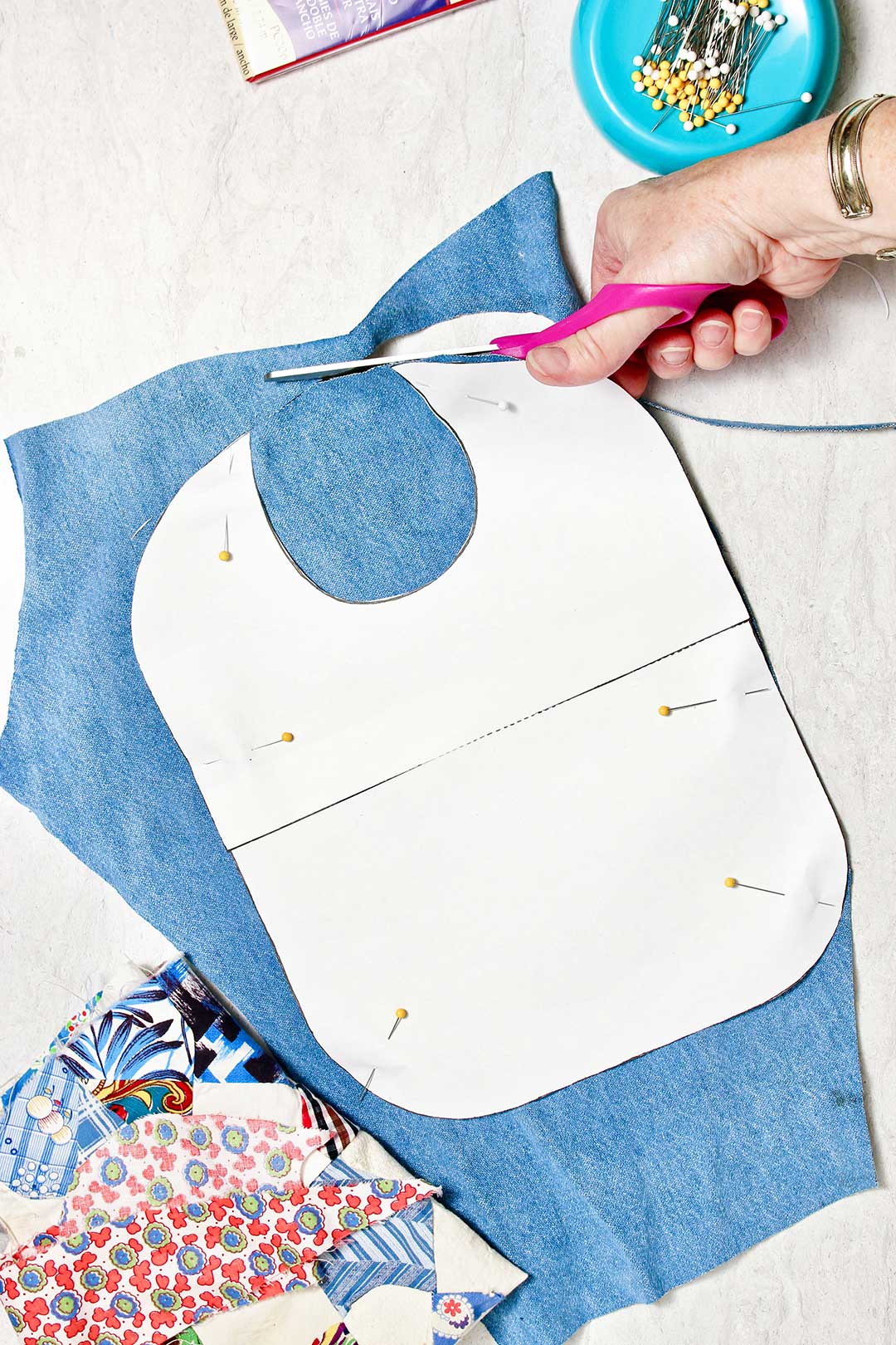 Hand cutting blue fabric for a bib base with white paper pattern pinned on top of it.