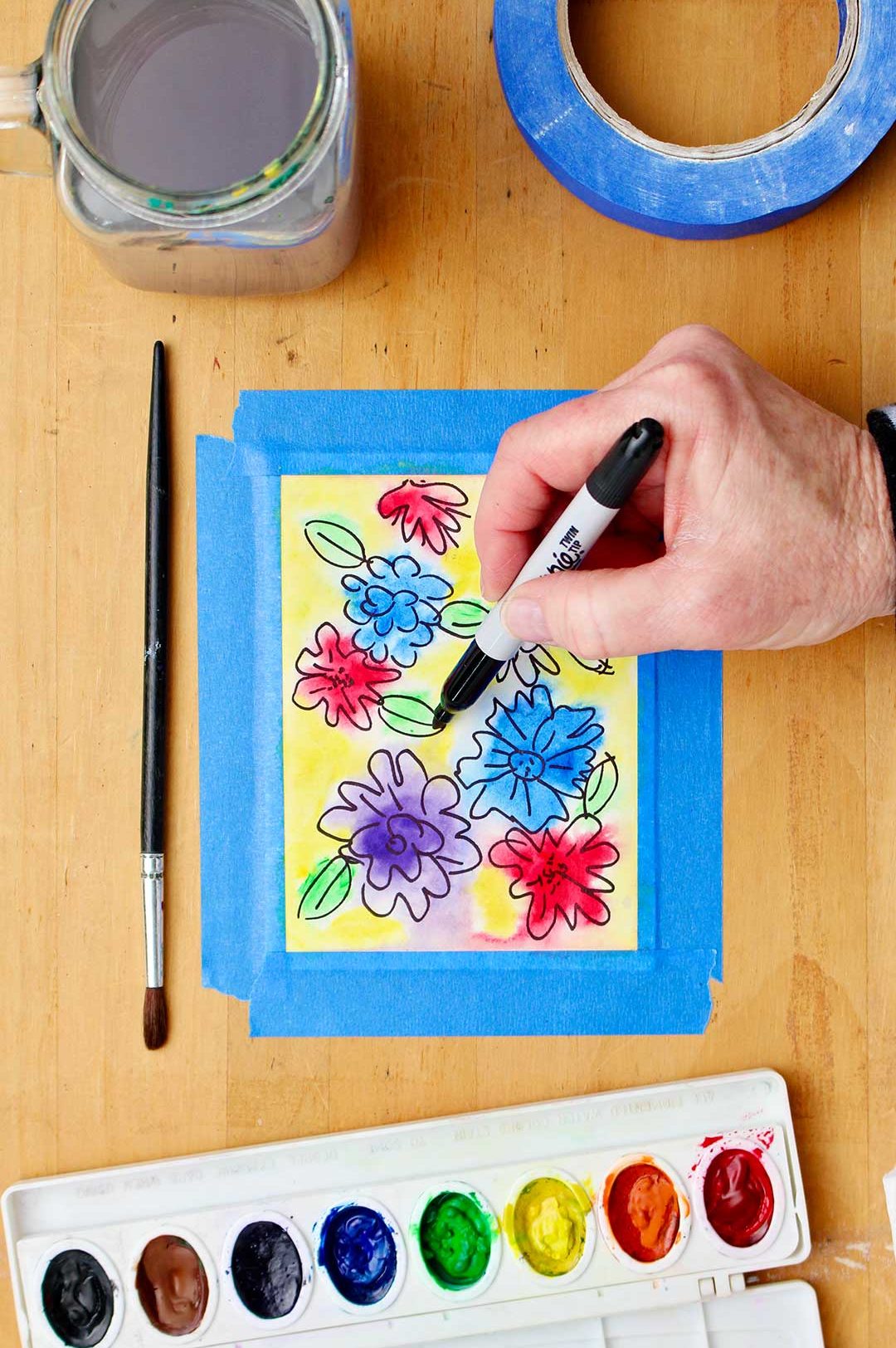 Hand outlining a leaf in the almost completed watercolor flower card.