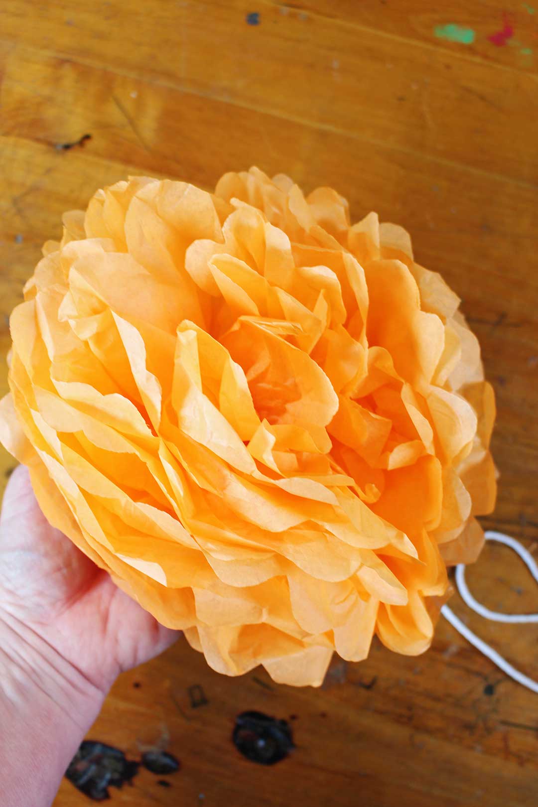 Hand holding up completed orange tissue paper flower.