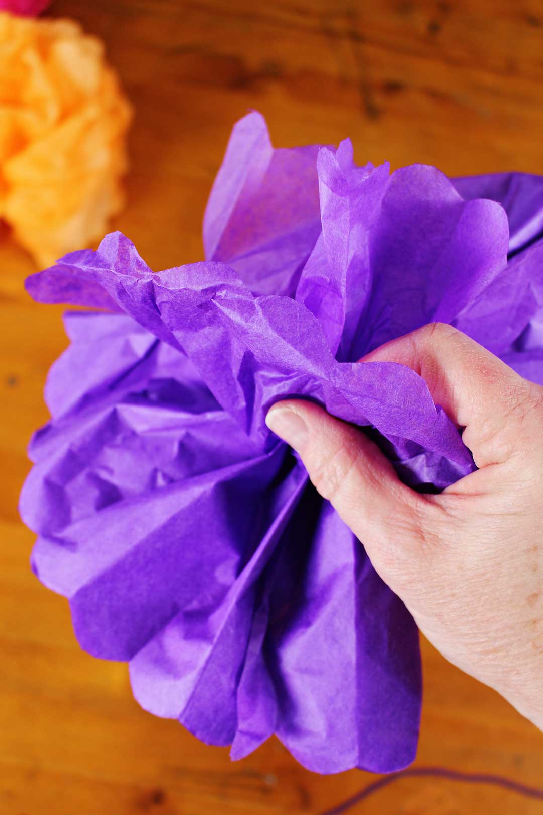 Hand fanning out and fluffing purple tissue paper flower.