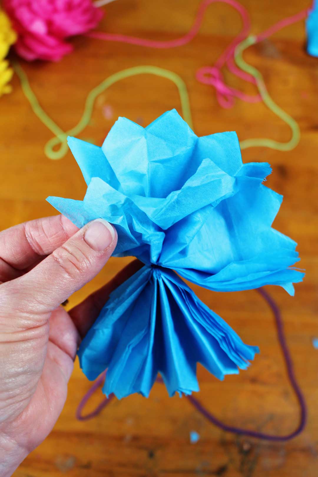 Hand fanning out blue tissue paper flower.