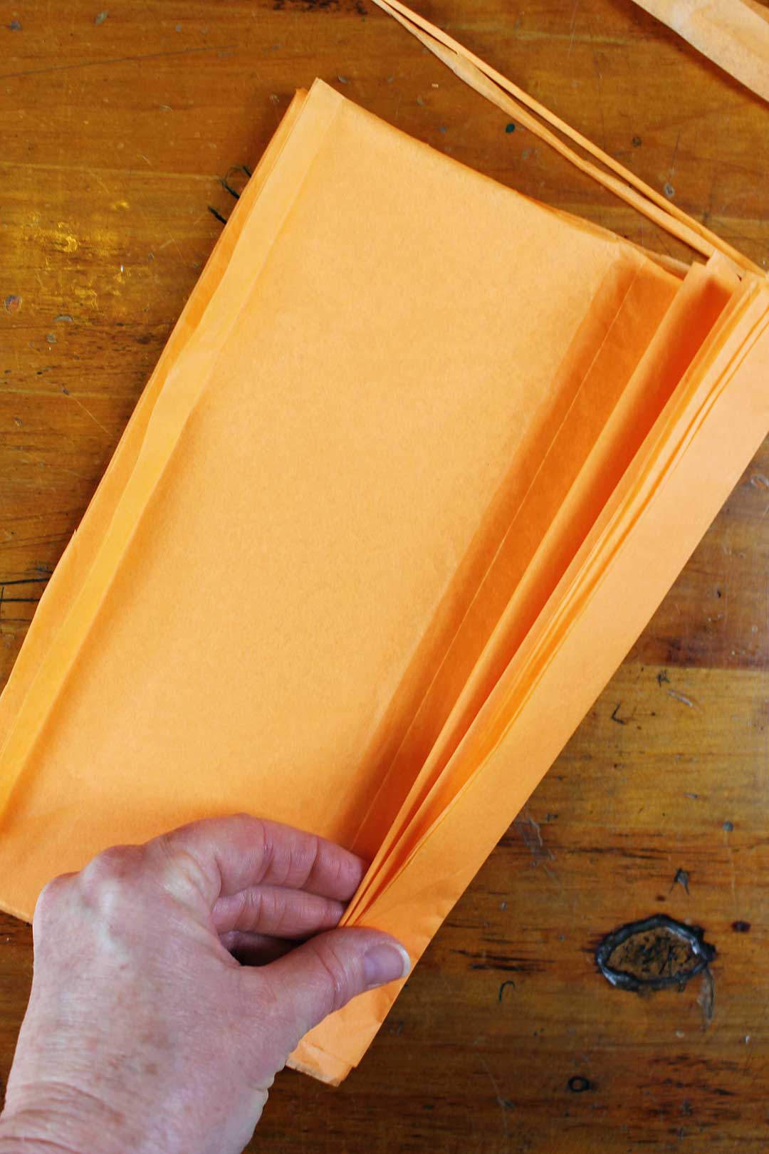 Hand folding a stack of orange tissue paper.