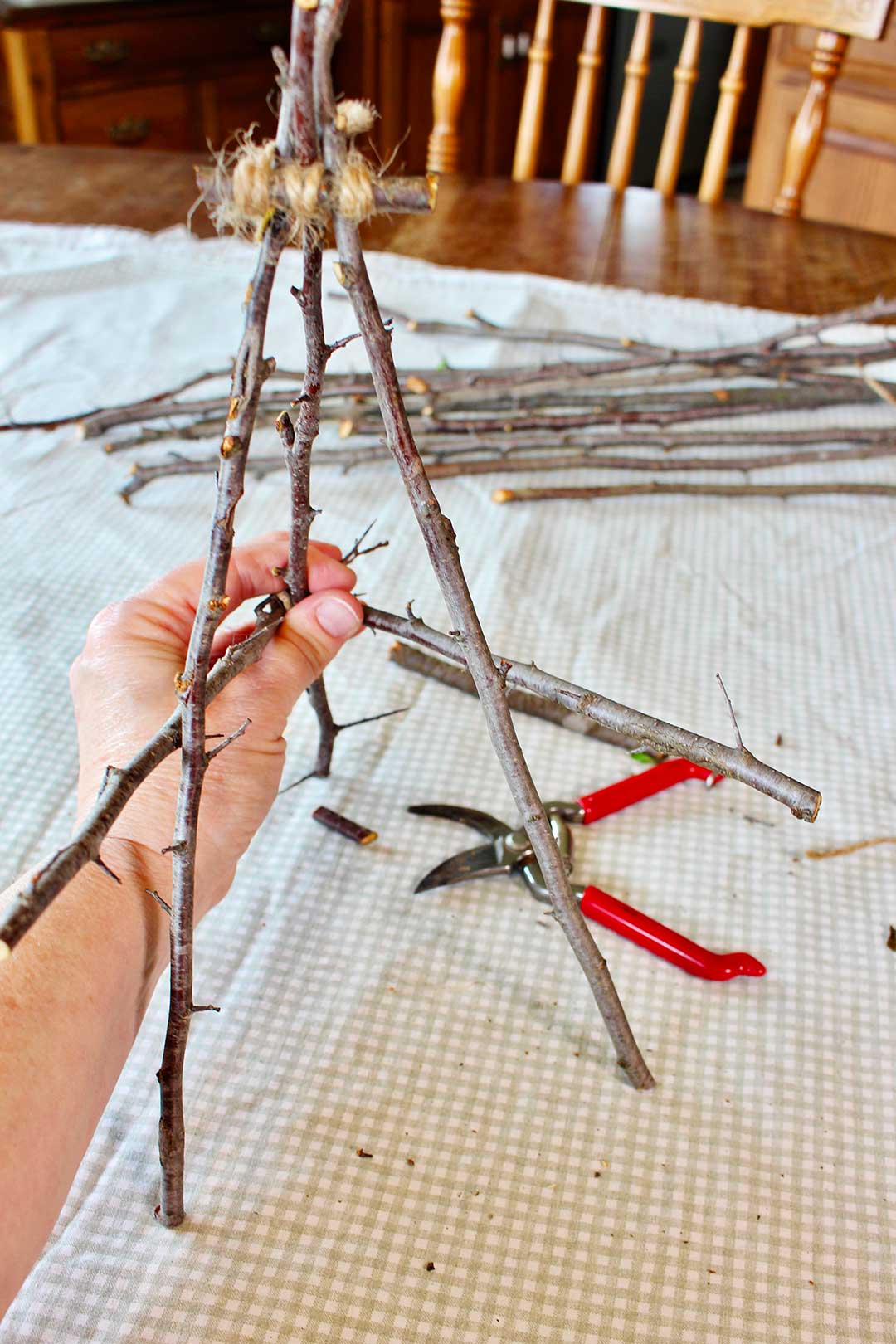 Hand holding the two side twigs of the easel to show how they should look before securing with twine.