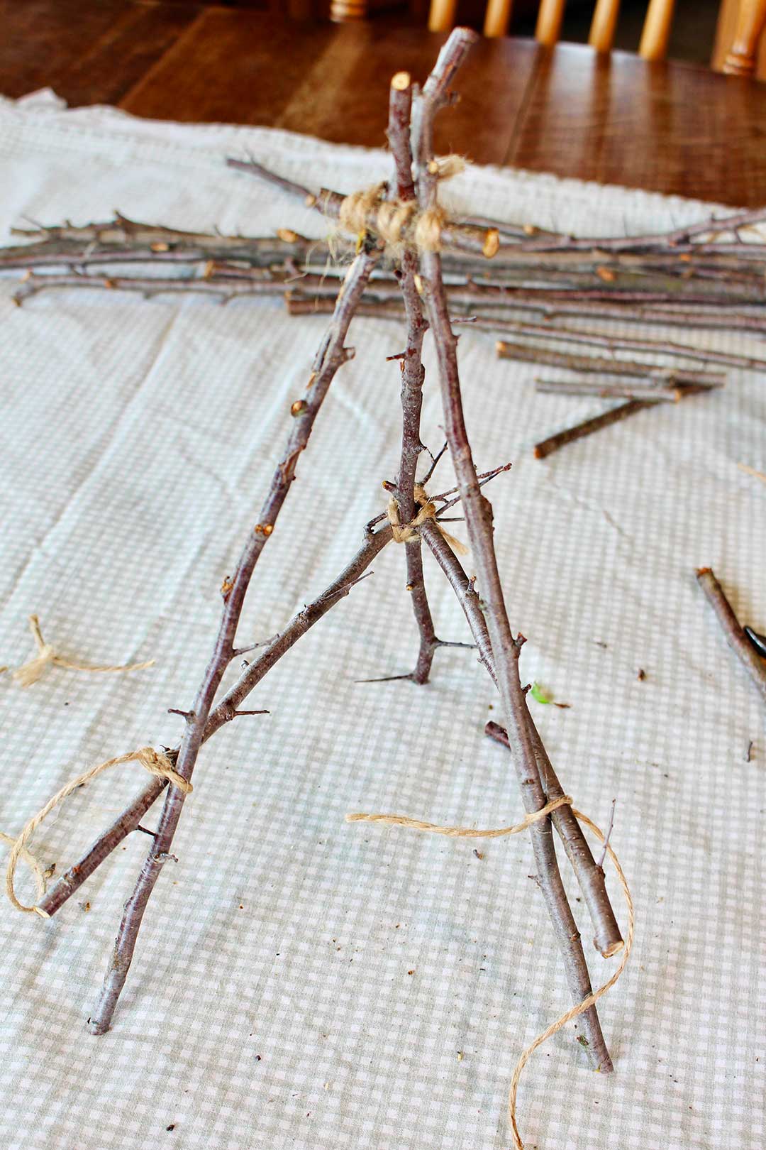 Semi completed easel made from twigs with a pile of twigs behind it on the kitchen table.