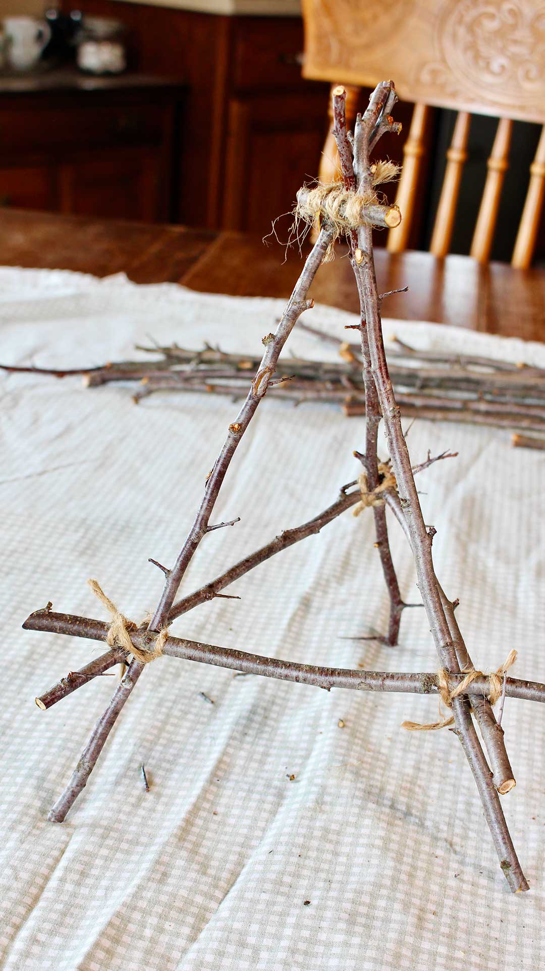 Completed tabletop easel from twigs sitting on a kitchen table draped with a piece of fabric.