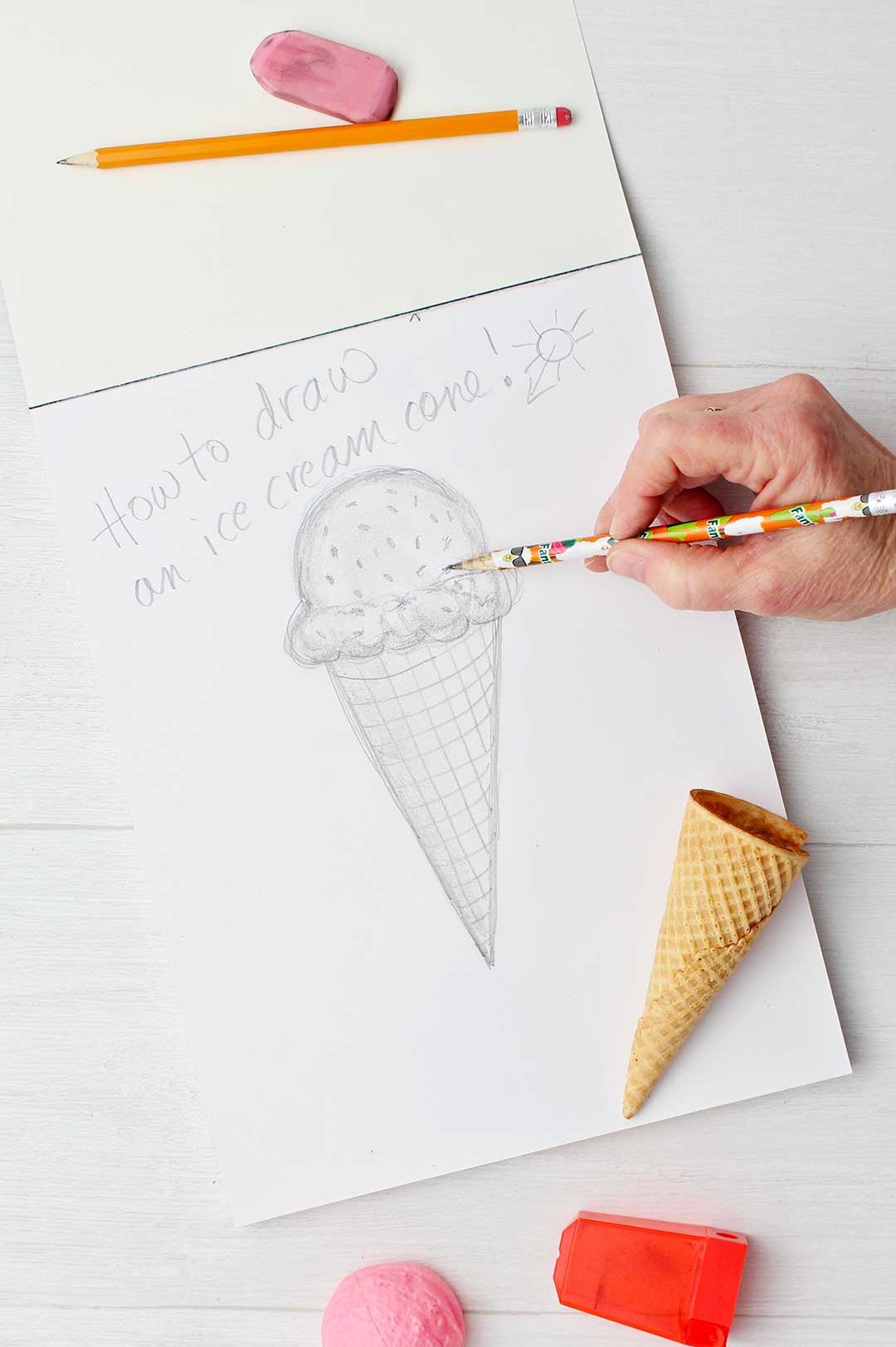Hand sketching final touches of sprinkles on ice cream cone sketch.