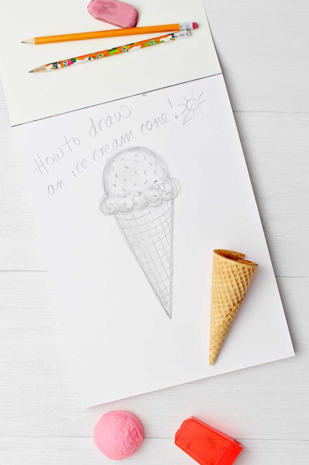 Completed sketch of an ice cream cone done in pencil with eraser, pencils and an ice cream cone resting near by.